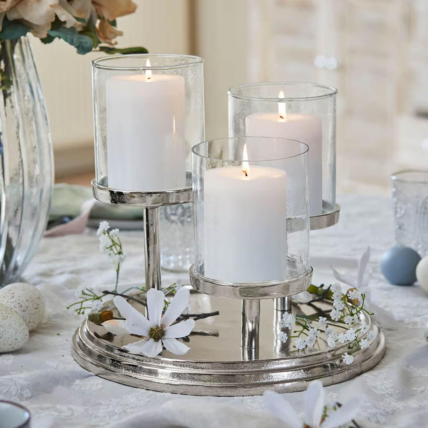 Portacandele triplo in metallo argentato con tre candele bianche e fiori decorativi sul tavolo