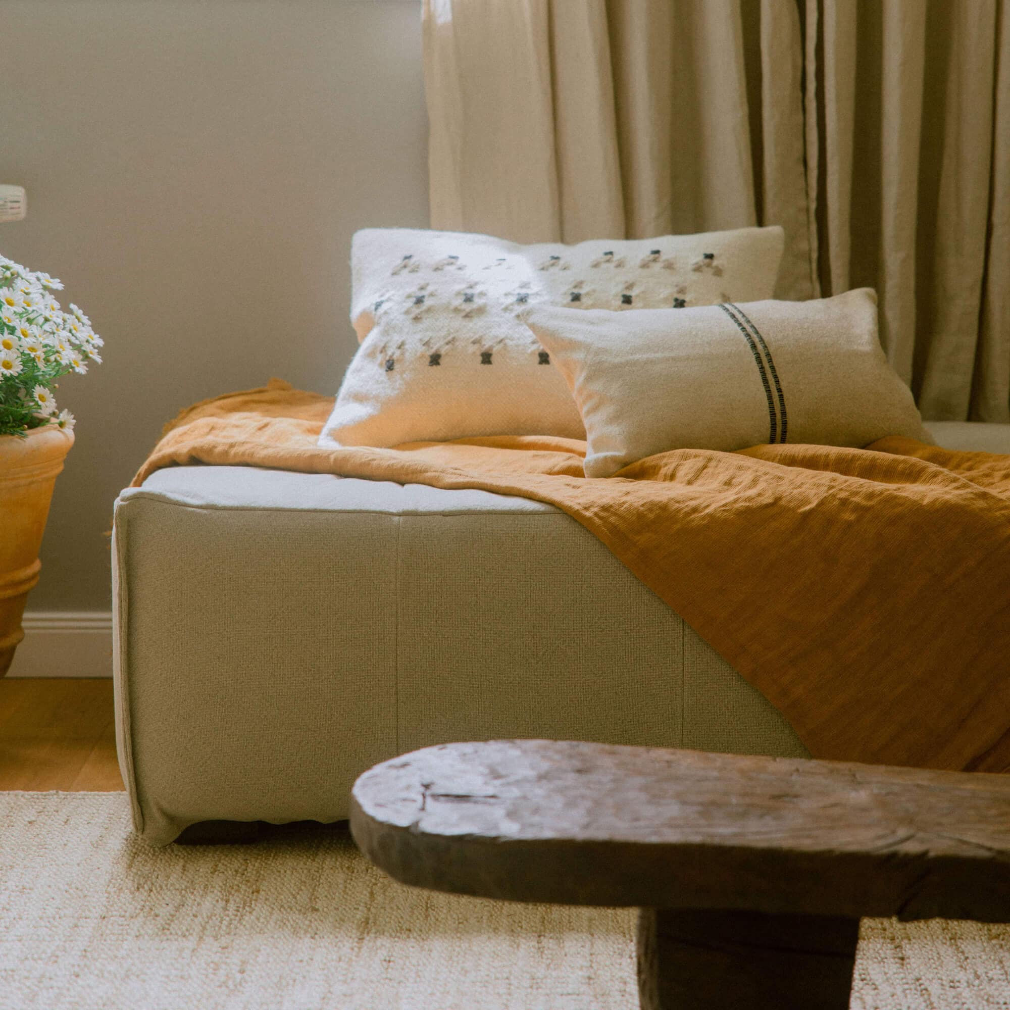 Pouf in tessuto beige con coperta arancione e cuscini decorativi in interno accogliente