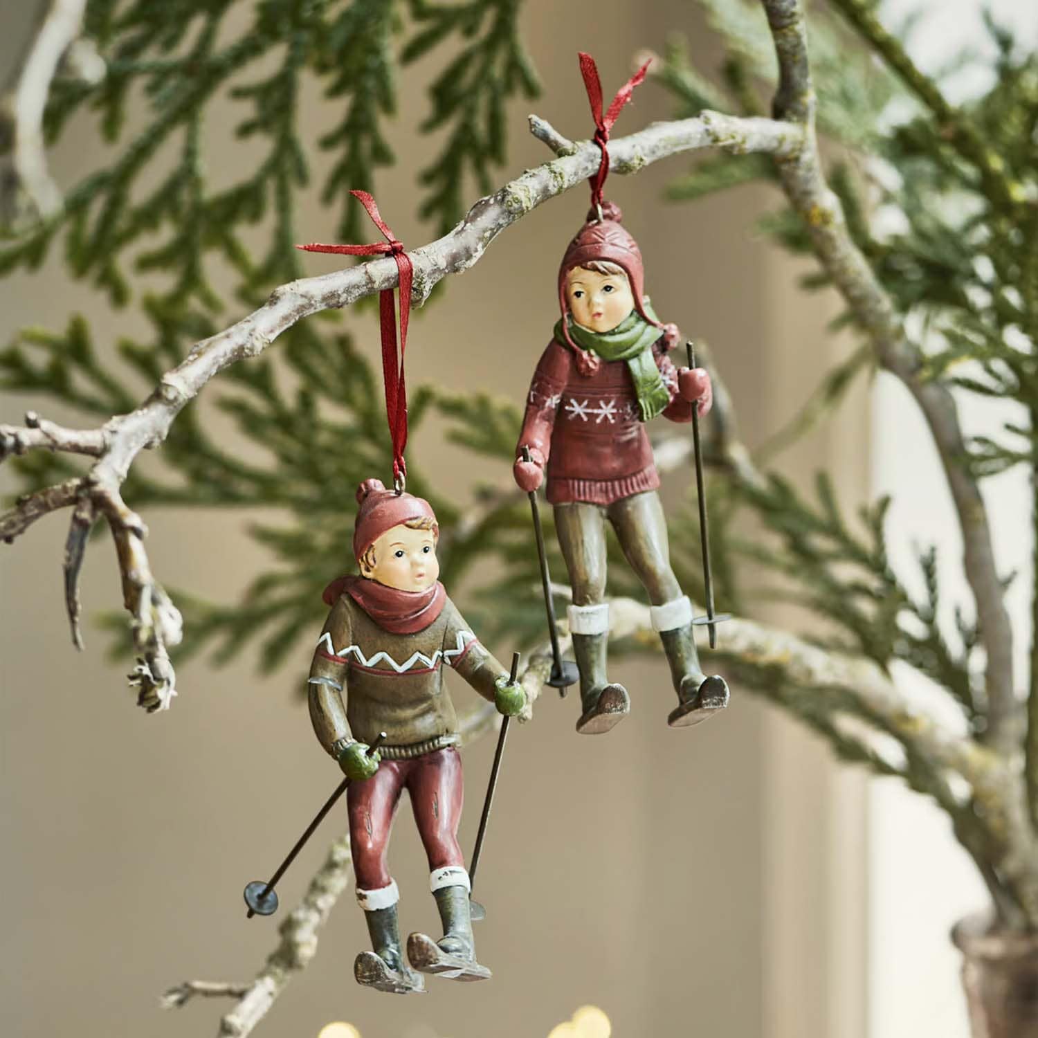 Due decorazioni appese con bambini sugli sci in abiti rossi e verdi su un ramo