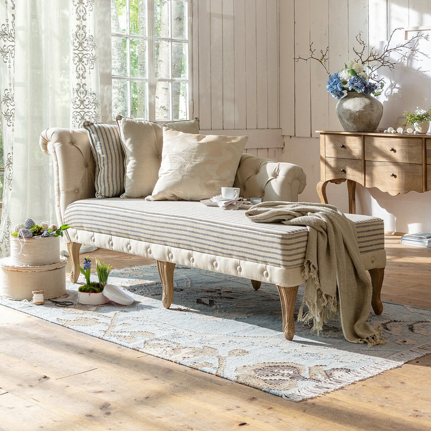 Chaise longue beige imbottita con gambe in legno e cuscini chiari in soggiorno luminoso
