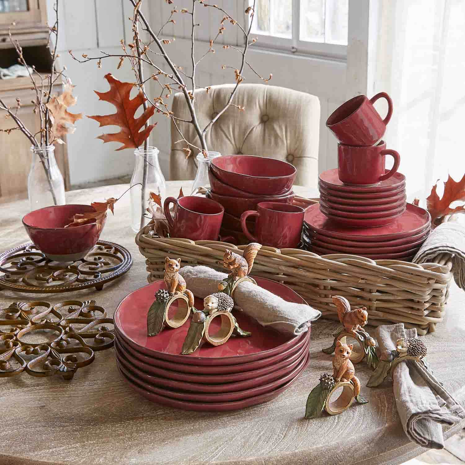 Set di stoviglie in ceramica rossa con tazze e piatti su tavolo in legno con decorazioni autunnali