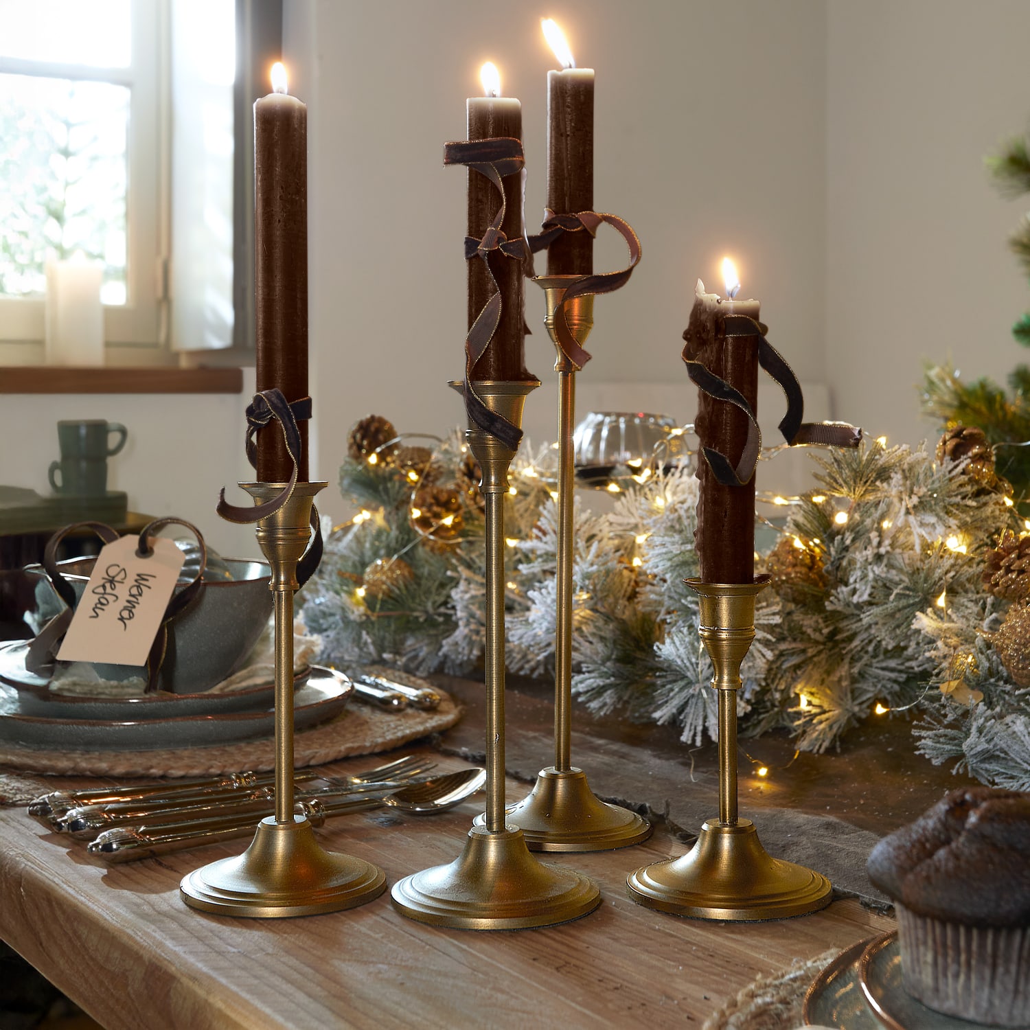 Set di quattro candelabri dorati con candele marroni e nastri decorativi su tavolo in legno