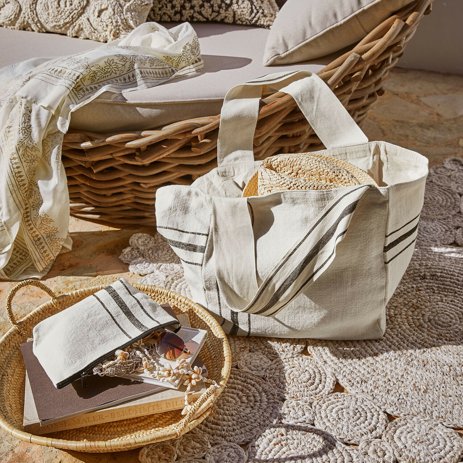 Set borsa e pochette Bravenda Borsa in cotone beige con righe e cappello di paglia su poltrona in vimini e tappeto