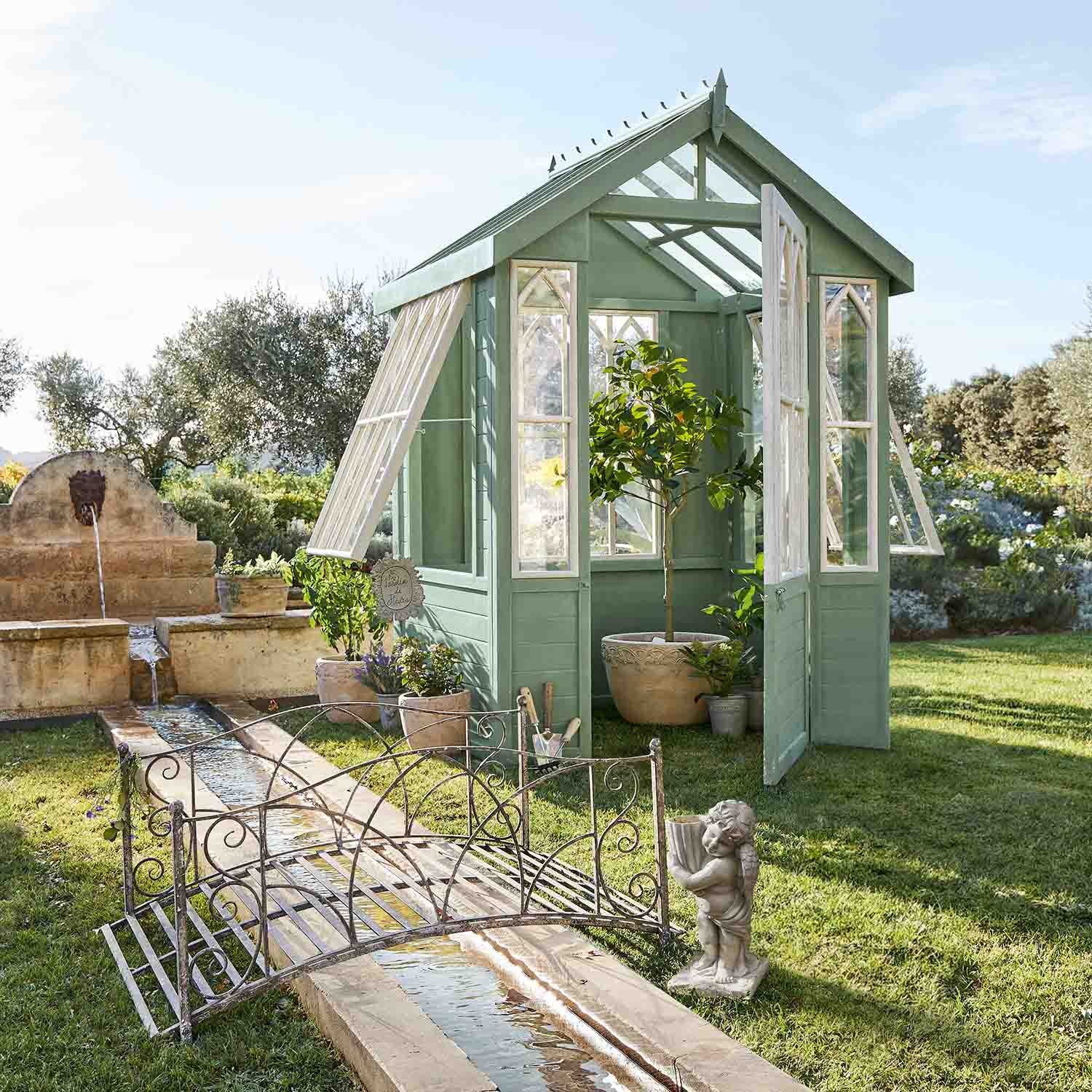 Serra in legno verde con finestre bianche in giardino con piante e fontana
