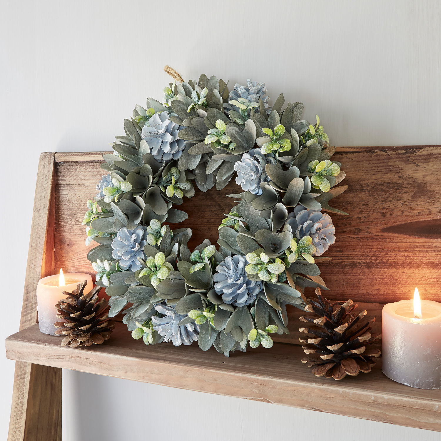 Ghirlanda Deinze Corona decorativa con foglie grigie e pigne blu su mensola in legno con candele e pigne