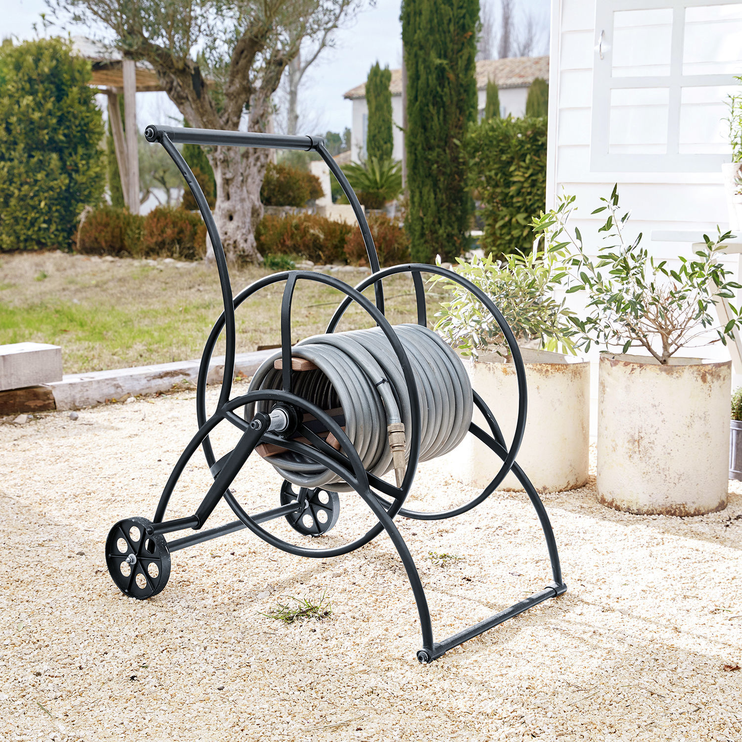 Carrello avvolgitubo Middleby Carrello in metallo nero con tubo da giardino grigio su ghiaia in giardino