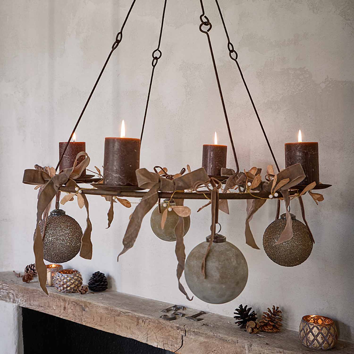 Candelabro sospeso in metallo con quattro candele marroni e sfere decorative su parete