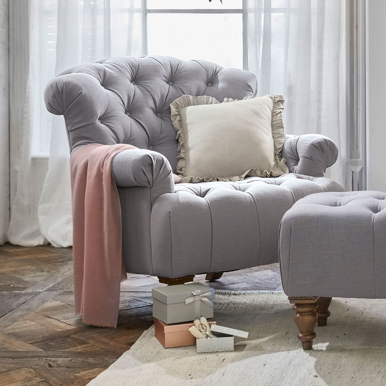Poltrona Springfield Poltrona grigia imbottita con poggiapiedi, cuscino crema e coperta rosa su pavimento in legno