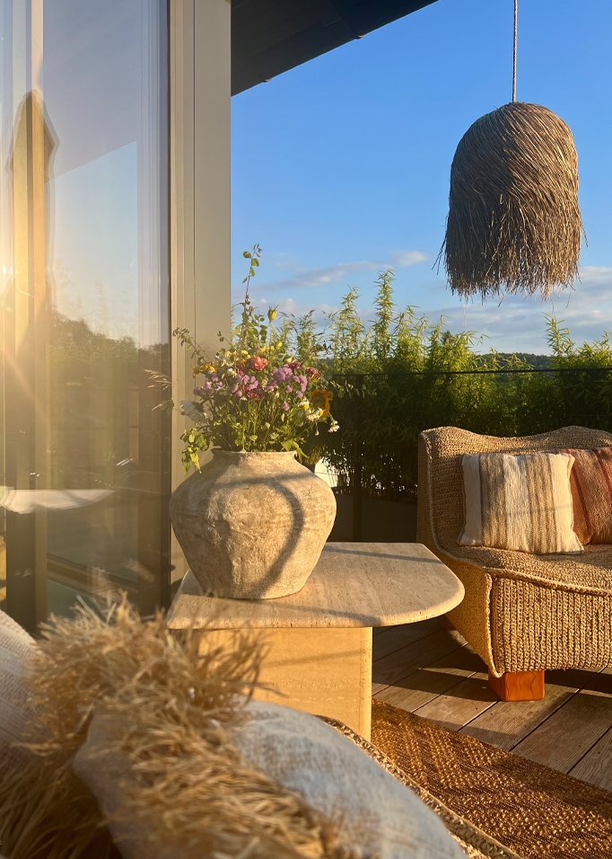 Accogliente balcone con poltrona in rattan, tavolo in pietra e vaso con fiori dai colori naturali