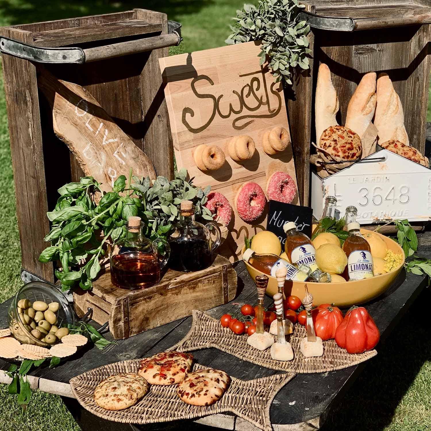 Tavolo rustico con cassette di legno, pane, olive, erbe aromatiche e limonata all'aperto al sole