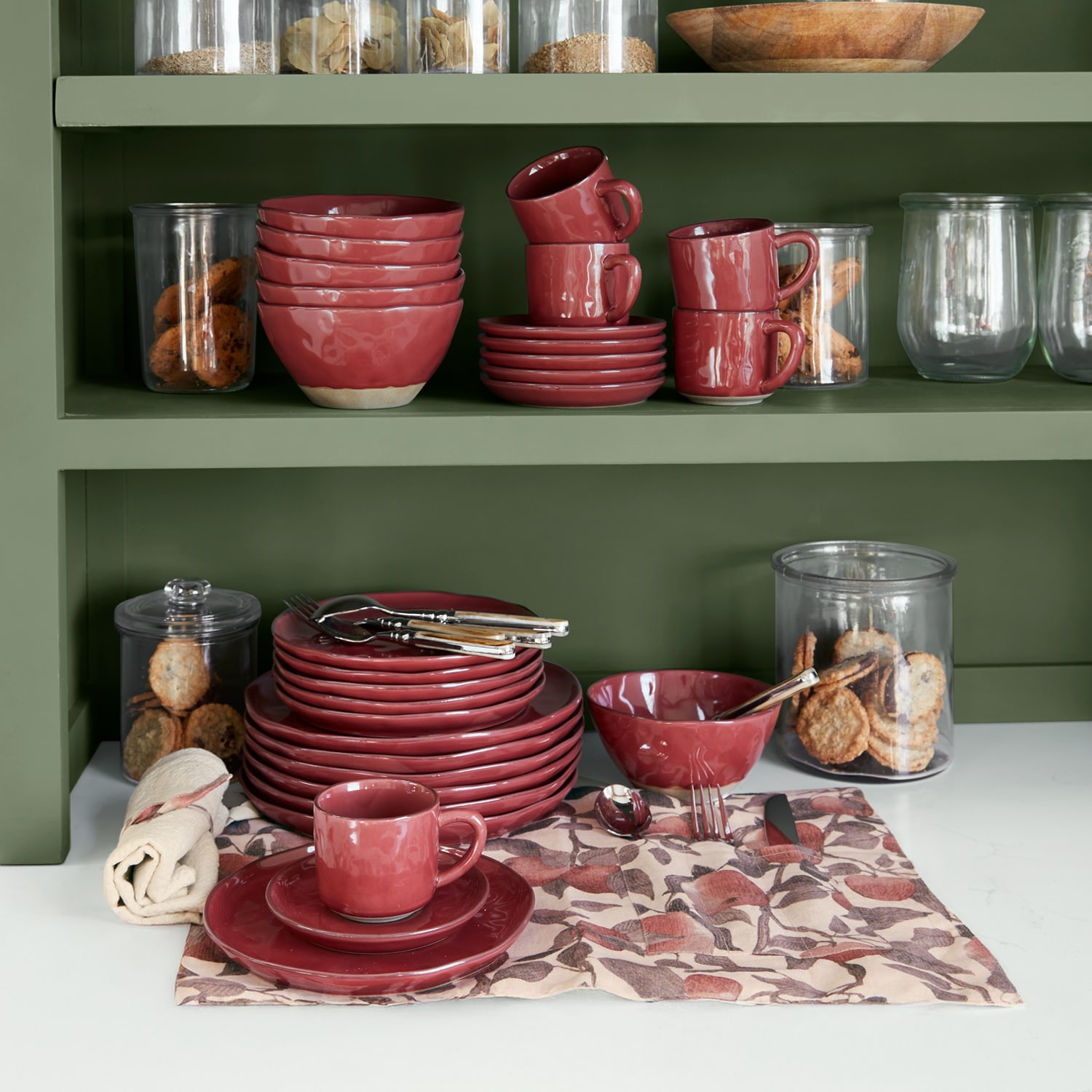 Set di stoviglie in ceramica rossa su mensola verde con biscotti in barattoli di vetro