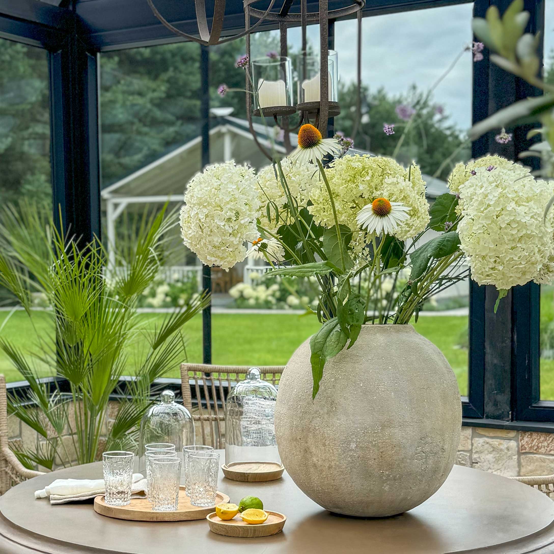 Grande vaso rotondo in cemento con fiori bianchi su tavolo in giardino, decorazione interna ed esterna