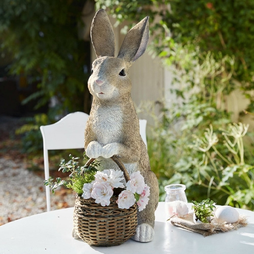 Coniglio decorativo in materiale sintetico colore naturale con cesto di vimini e fiori su tavolo da giardino