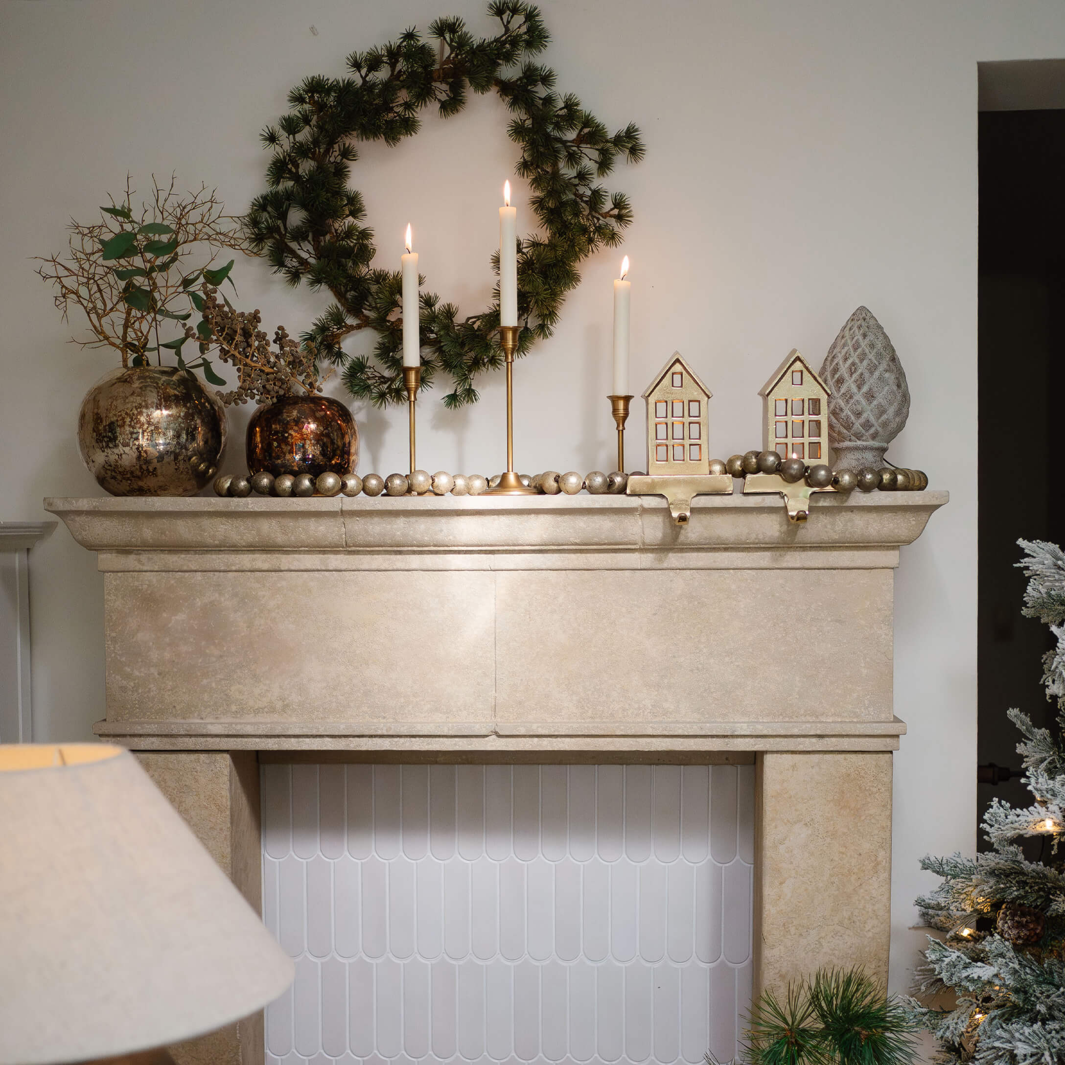 Camino in pietra beige con corona verde, candelabri dorati e decorazioni natalizie eleganti