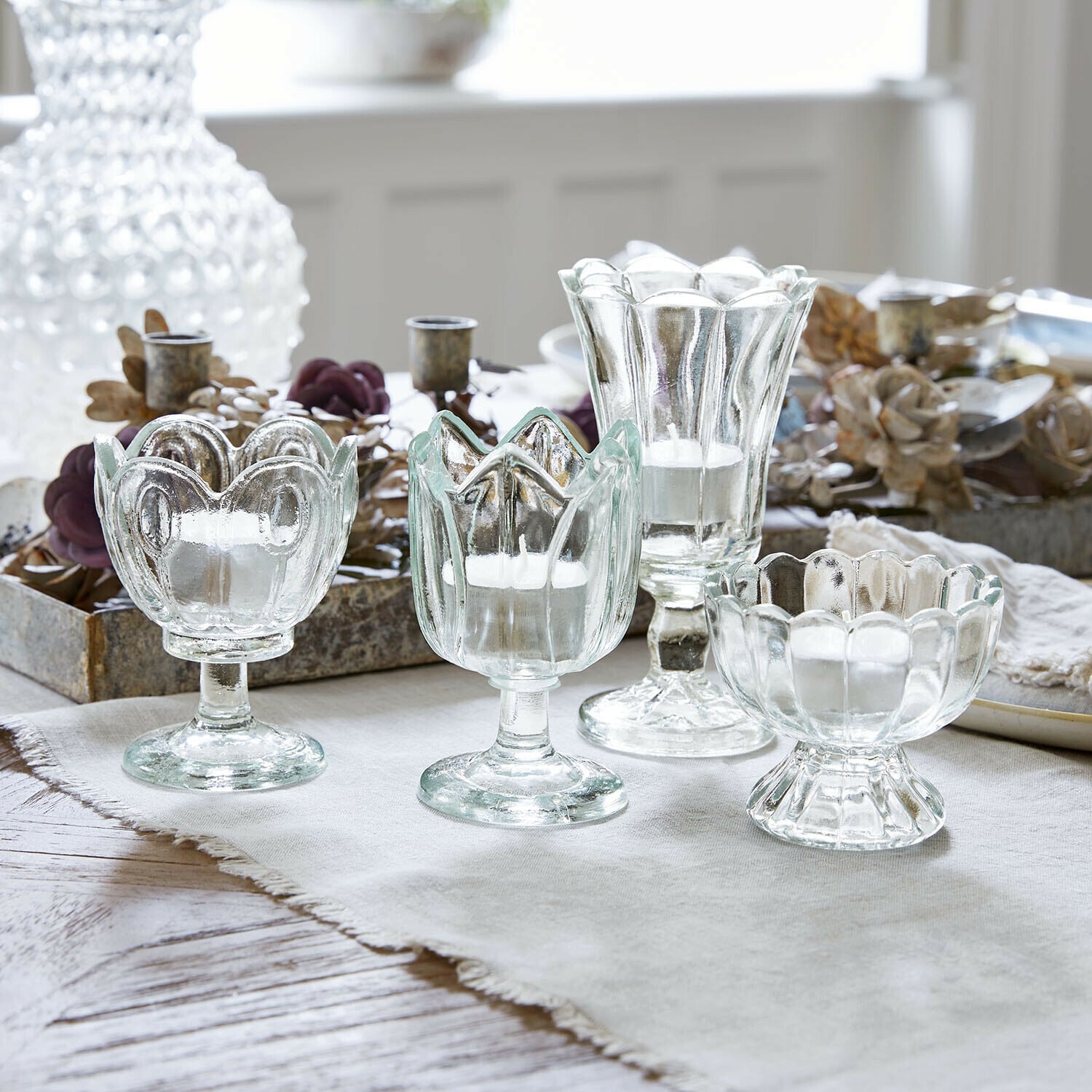 Set di 4 portalumini Amisette Set di quattro portacandele in vetro trasparente di forme diverse su tovaglia chiara