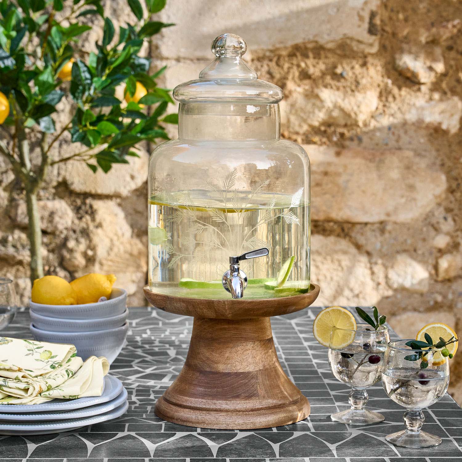 Dispenser per bevande in vetro con coperchio su base in legno con acqua e fette di limone