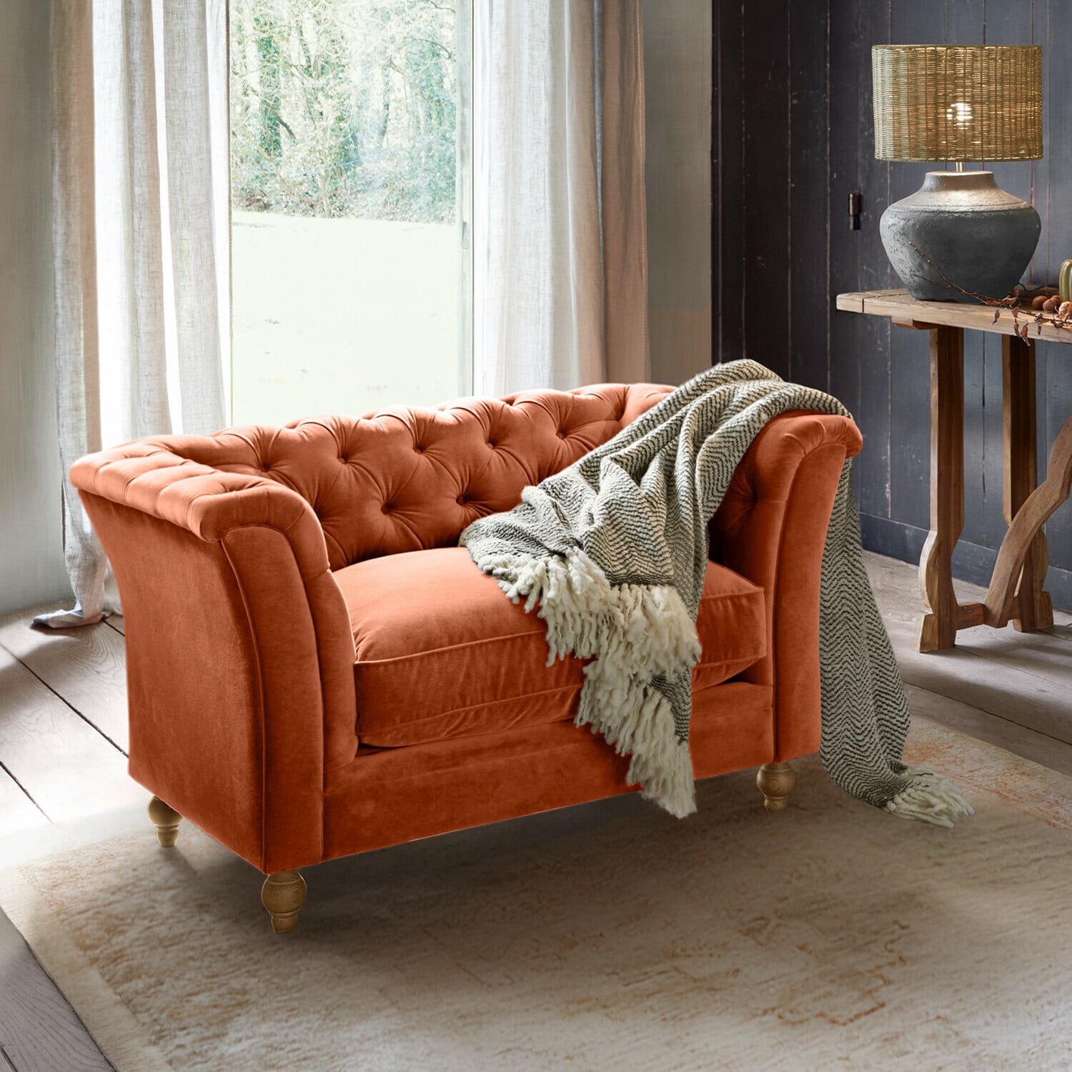 Divano Chesterfield arancione in velluto con coperta grigia in soggiorno accogliente con lampada e tavolo in legno