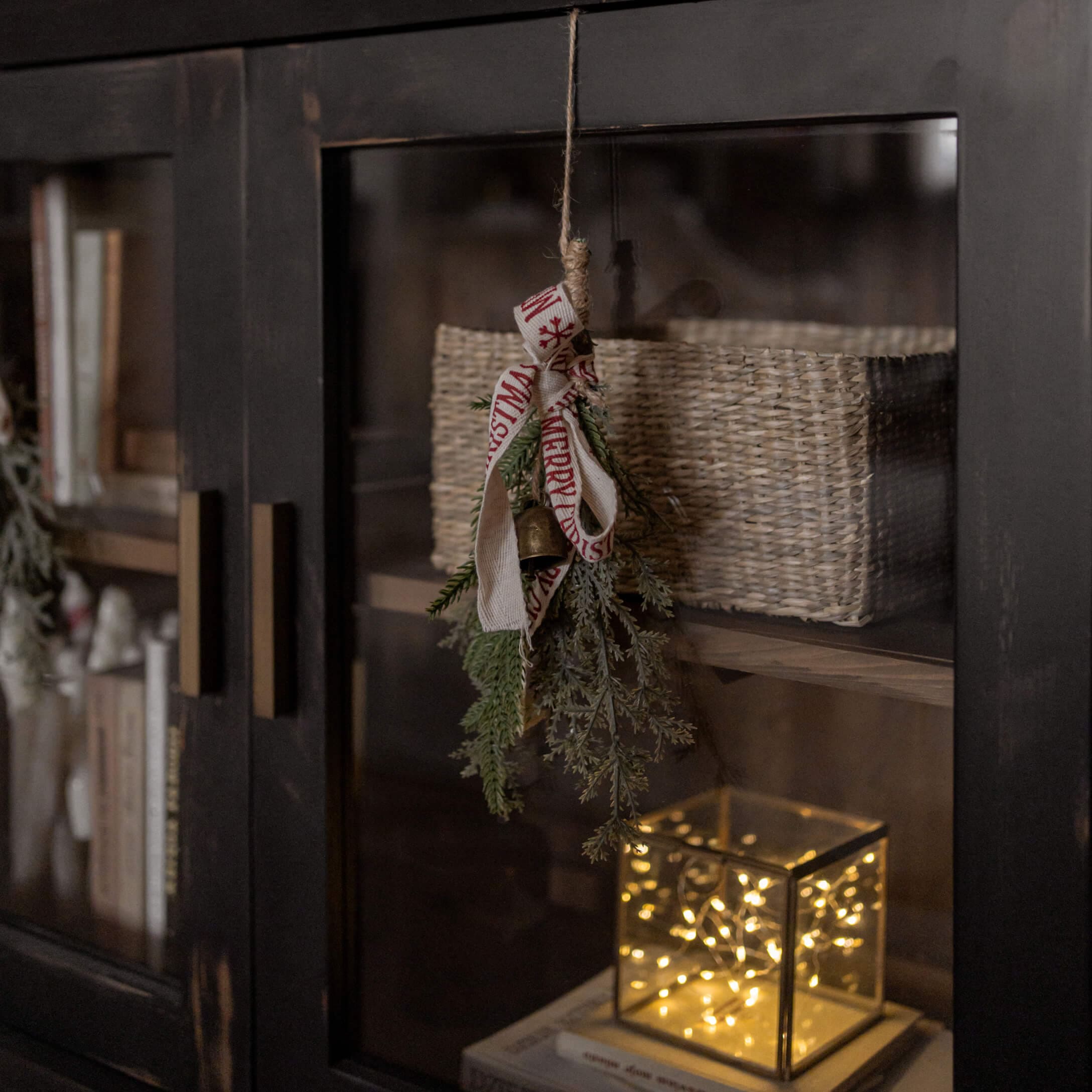 Decorazione natalizia con rami verdi, campanella e nastro su mobile nero con cesta e luce LED