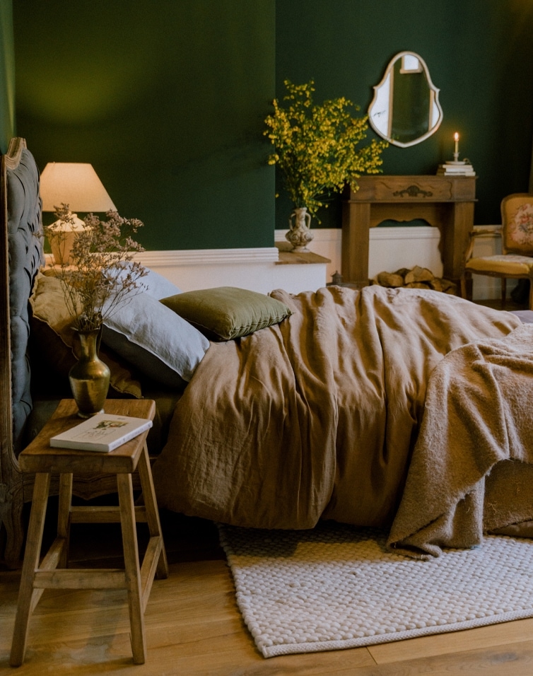 Camera accogliente con biancheria da letto in lino marrone e cuscini verdi su parete verde scuro
