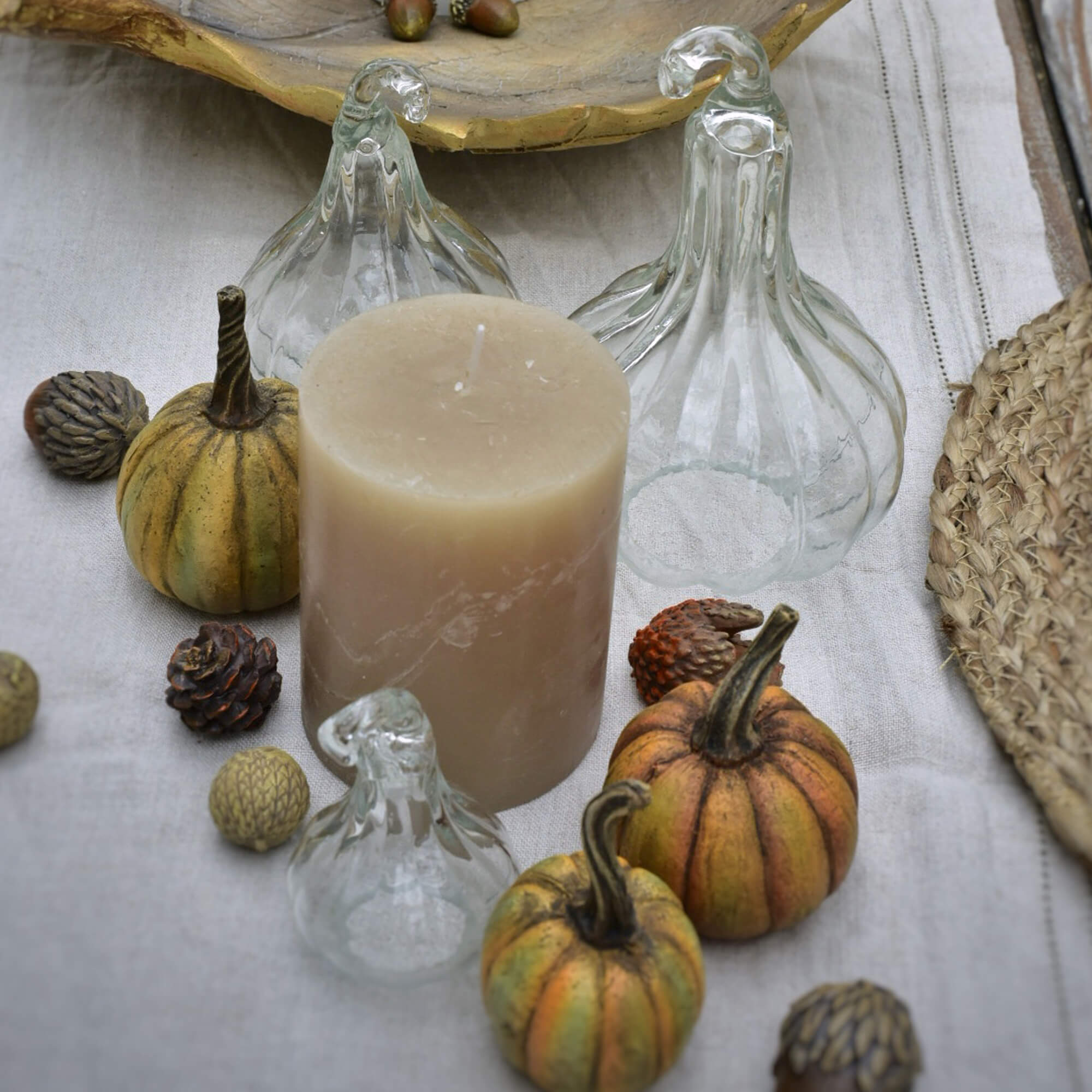 Candela beige con zucche di vetro decorative e piccole decorazioni su tessuto di lino
