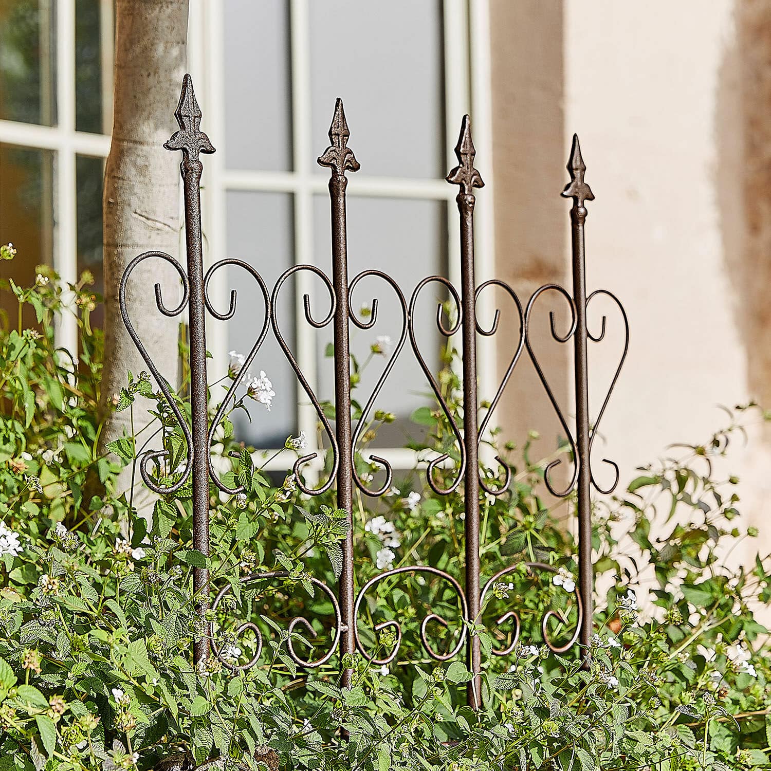 Traliccio per rampicanti Nectarise Recinzione da giardino in metallo marrone ruggine con motivo a cuore, circondata da piante verdi e fiori bianchi