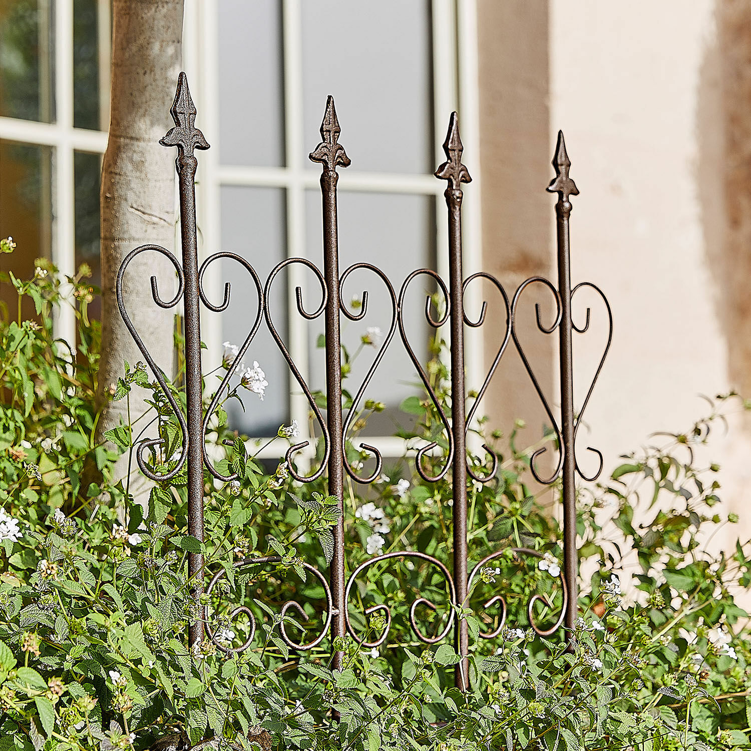 Traliccio per rampicanti Nectarise Recinzione da giardino in metallo marrone ruggine con motivo a cuore, circondata da piante verdi e fiori bianchi