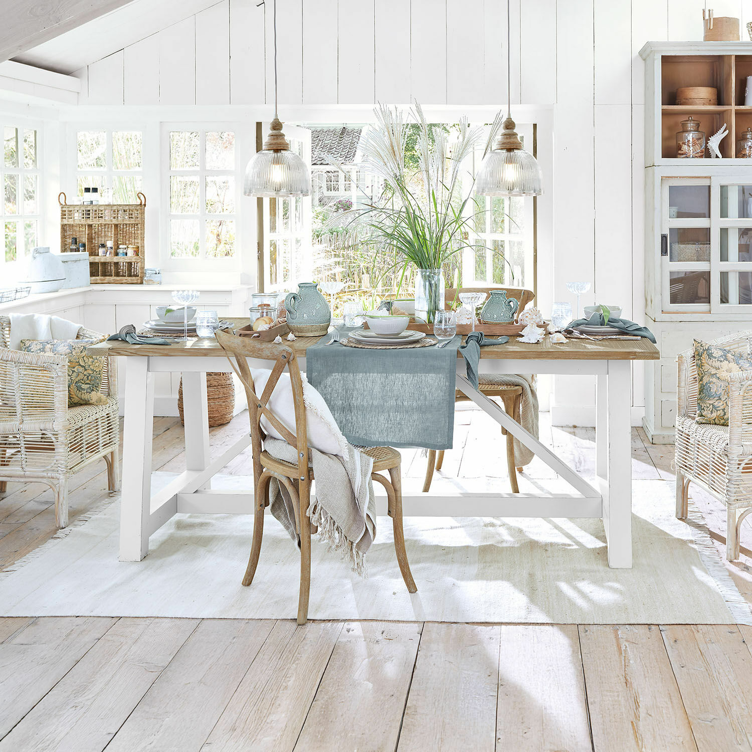 Tavolo da pranzo Dubberly Sala da pranzo rustica con tavolo in legno, sedie in vimini, decorazioni naturali e luce naturale