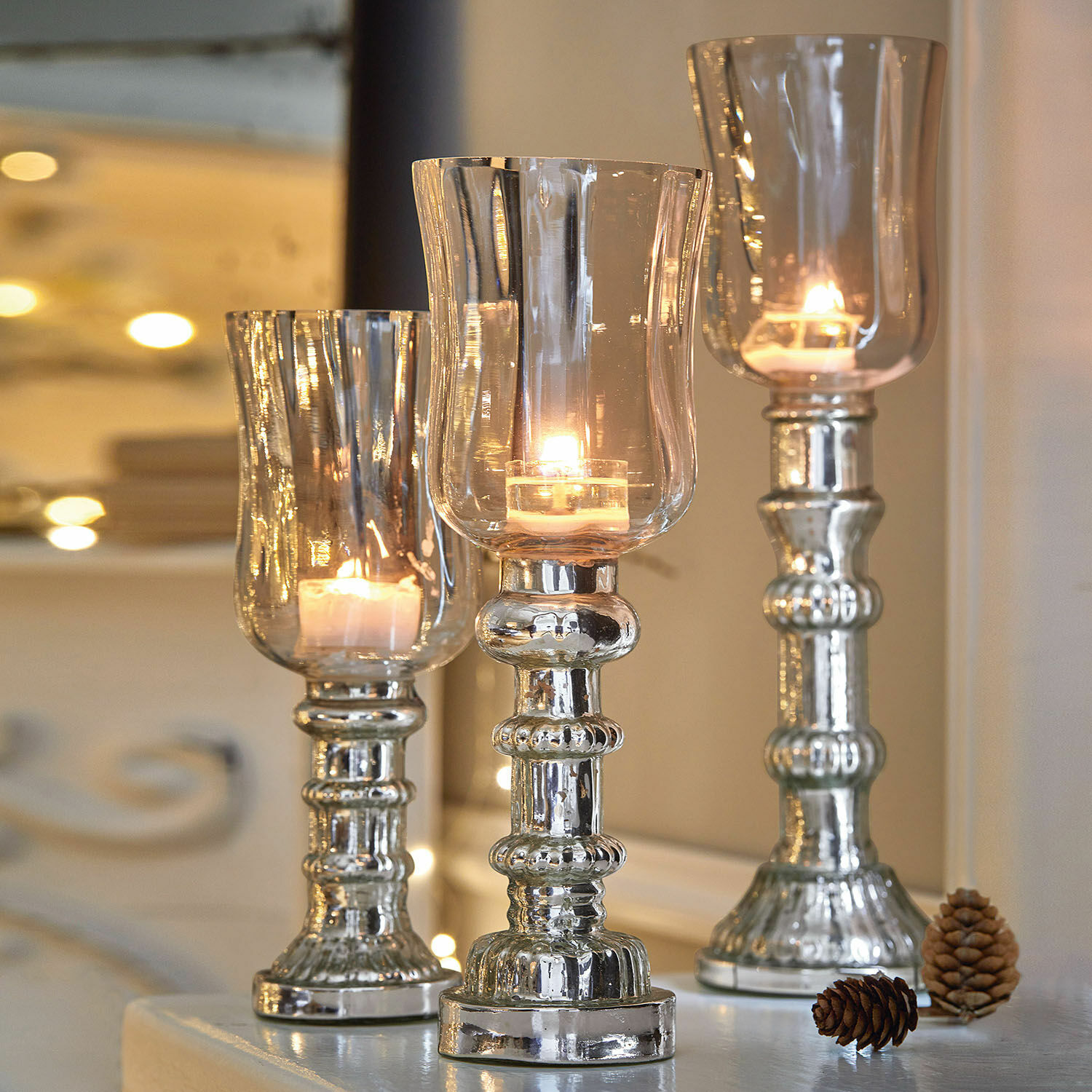 Set di 3 portacandele Fréjeville Set di tre portacandele argentati in vetro e metallo con candele accese e pigne decorative