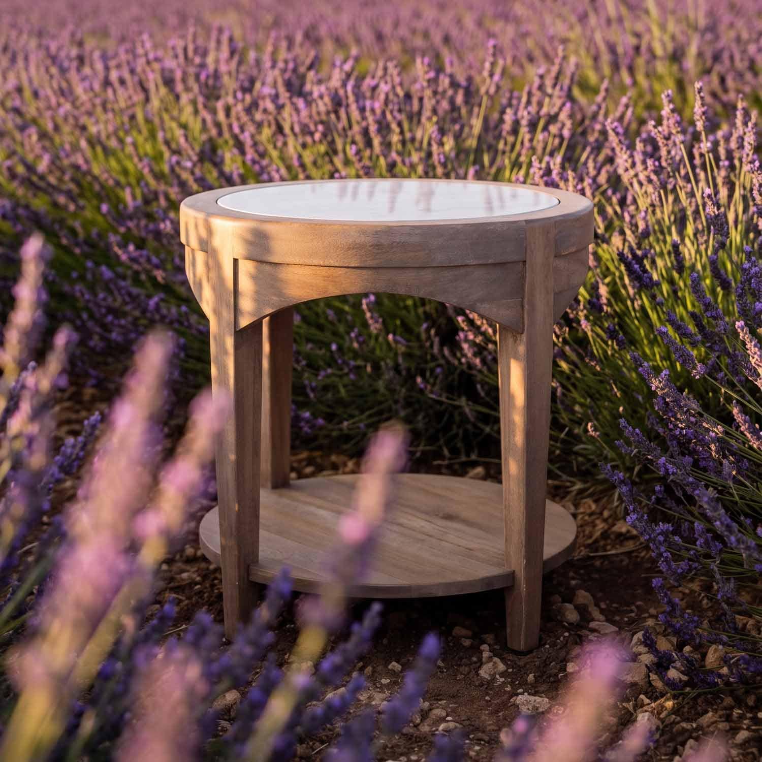 Tavolino rotondo in legno con piano bianco, posizionato tra fiori di lavanda viola all'aperto