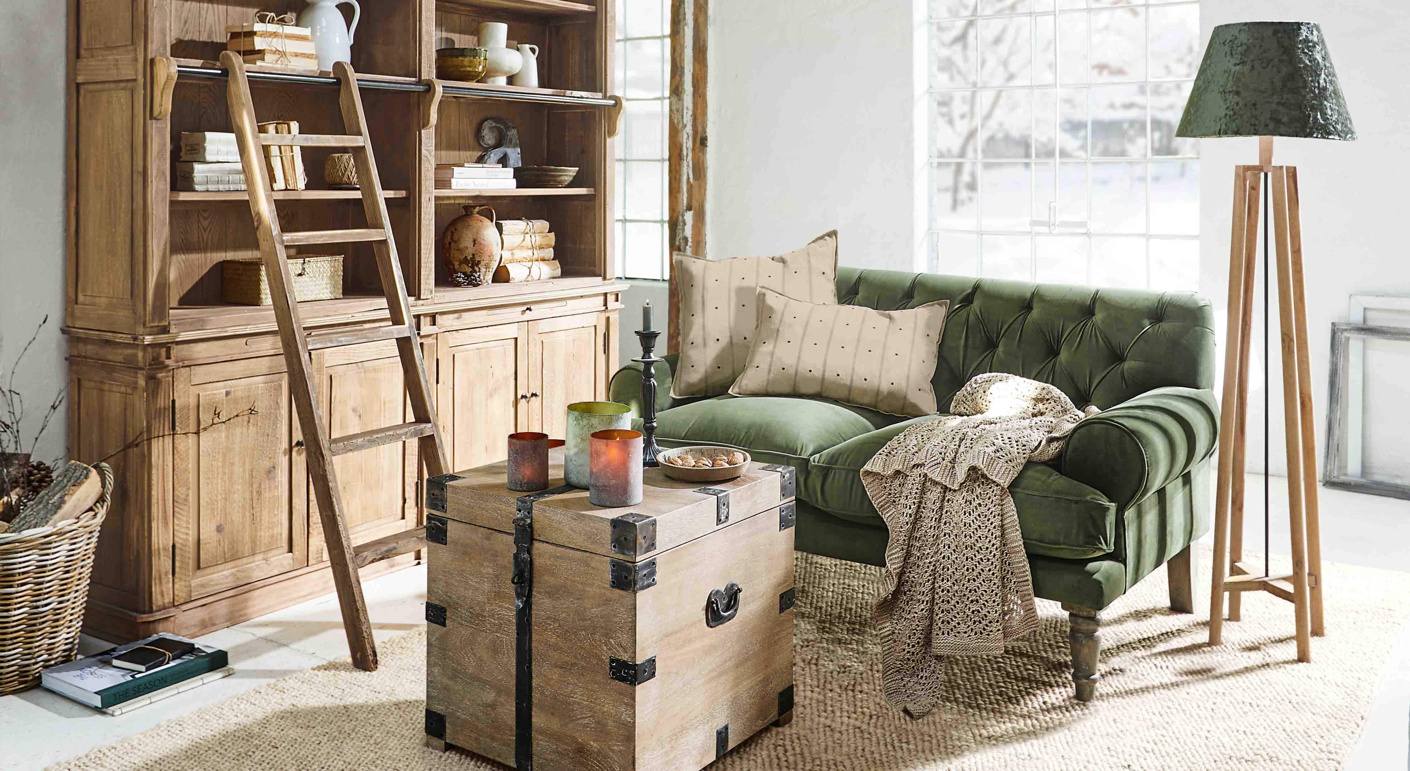 Soggiorno accogliente con divano verde in velluto, armadio in legno e lampada da terra in legno naturale