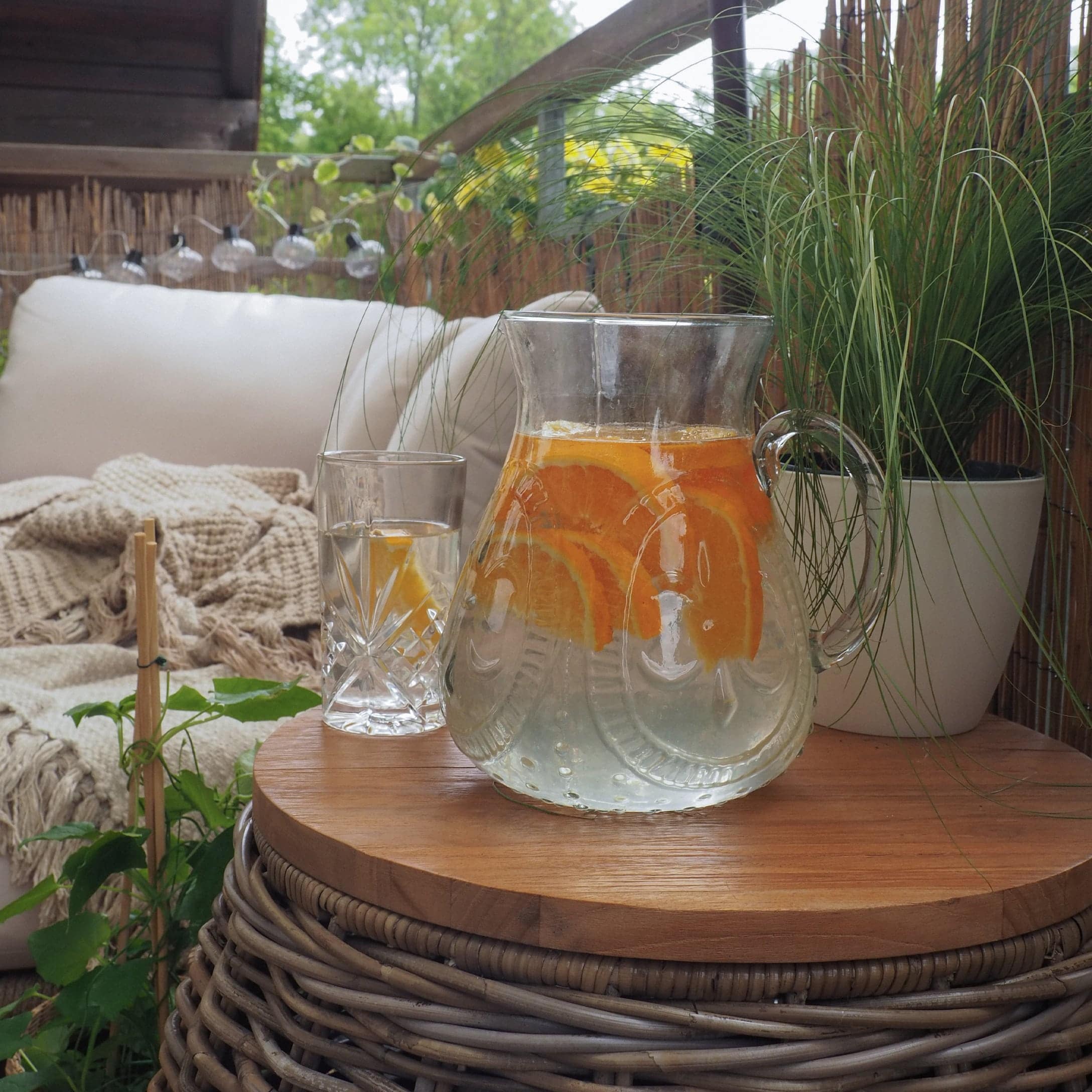 Caraffa di vetro con acqua e fette d'arancia su tavolo in legno su terrazza con piante