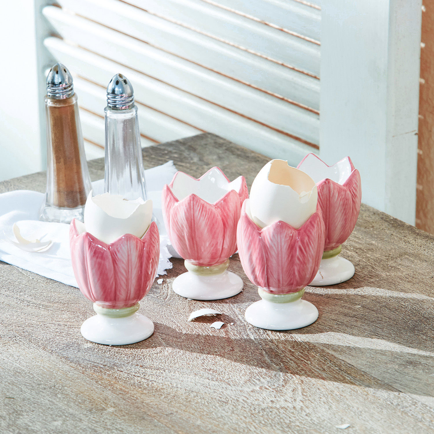 Set di 4 portauova Mireille Portauova in ceramica rosa a forma di tulipano su tavolo in legno con saliera e pepiera