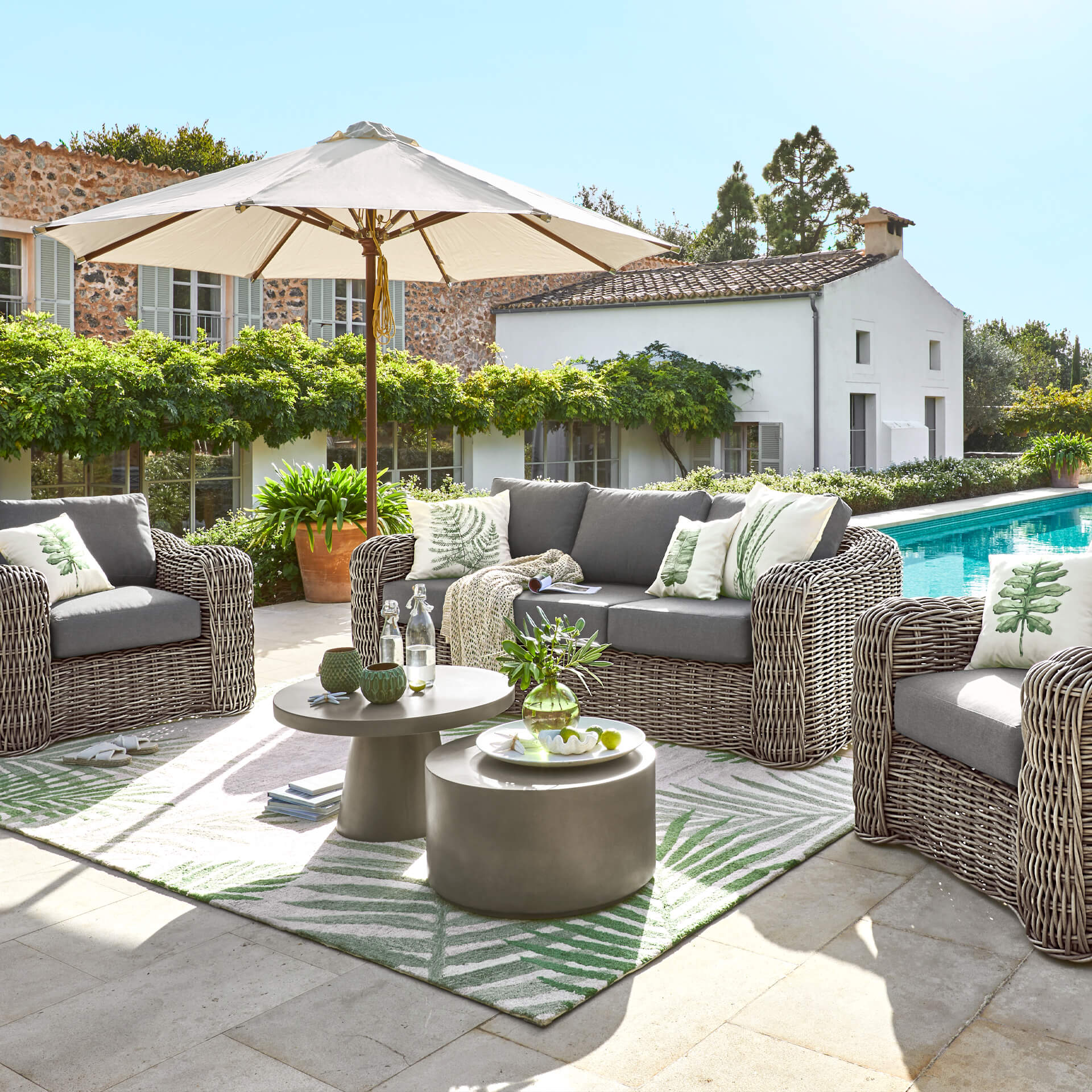 Set di mobili da giardino in tecnorattan grigio con cuscini e ombrellone vicino alla piscina
