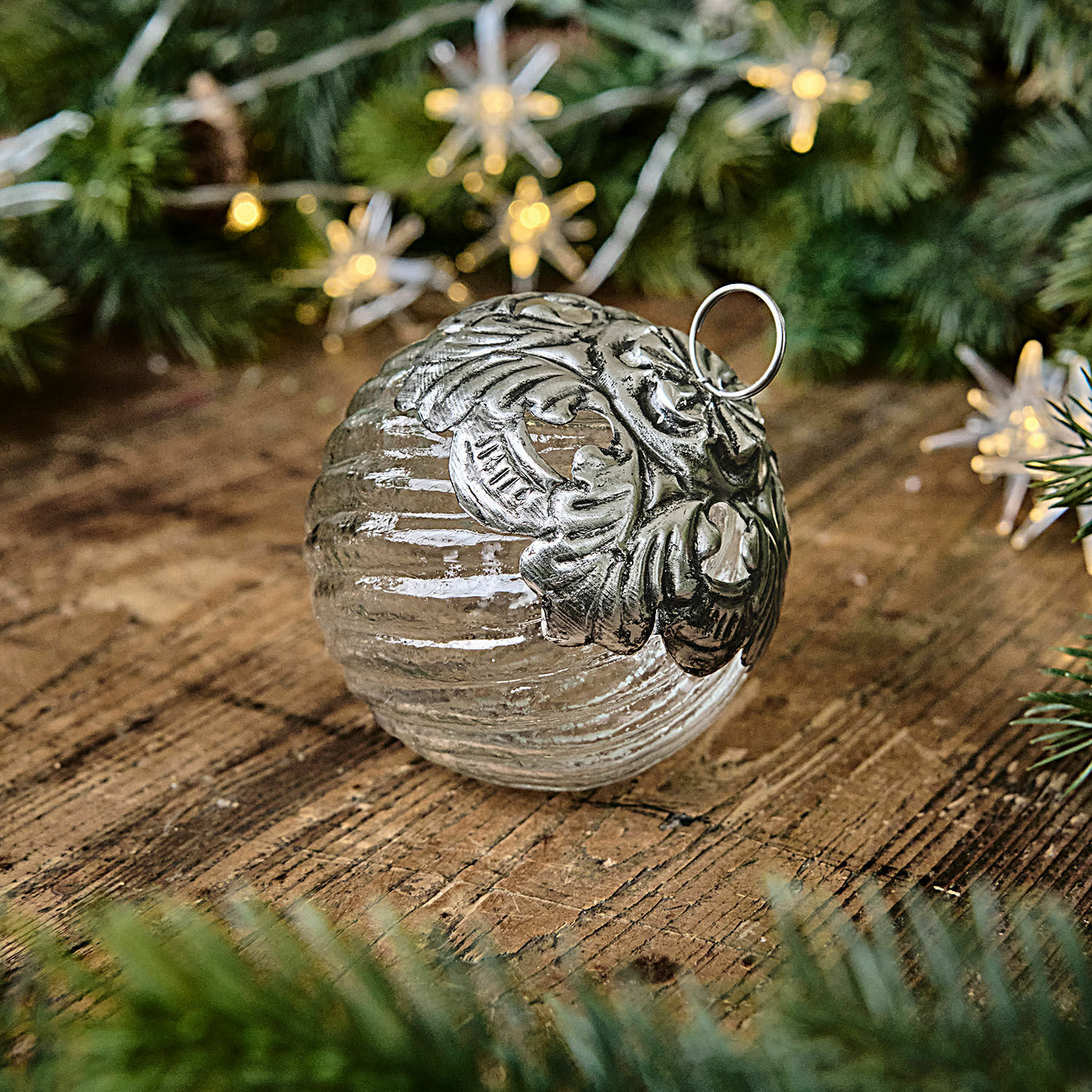 Pallina di Natale Zoriline Pallina di Natale in vetro con decorazione metallica argento su tavolo in legno con rami verdi