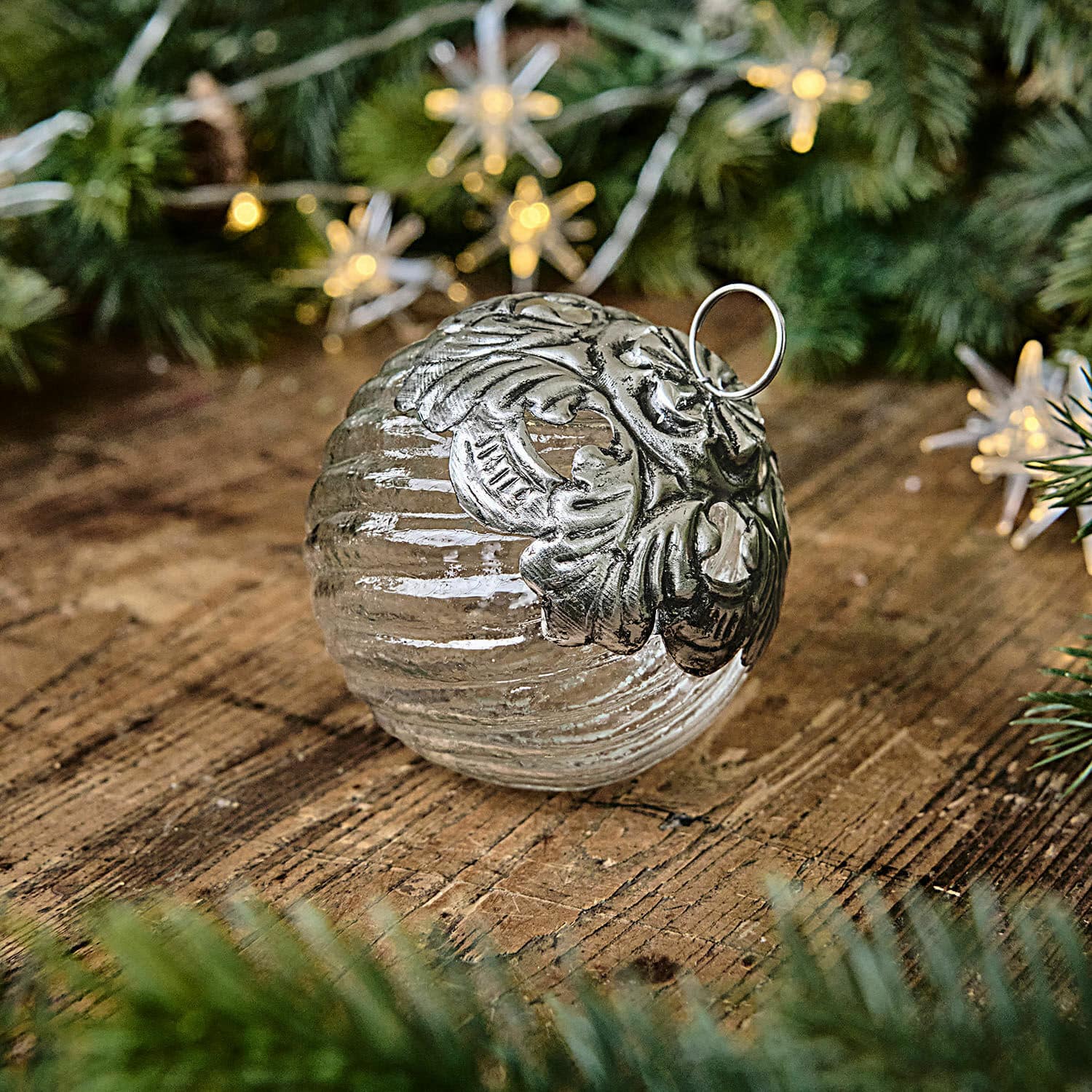 Pallina di Natale Zoriline Pallina di Natale in vetro con decorazione metallica argento su tavolo in legno con rami verdi