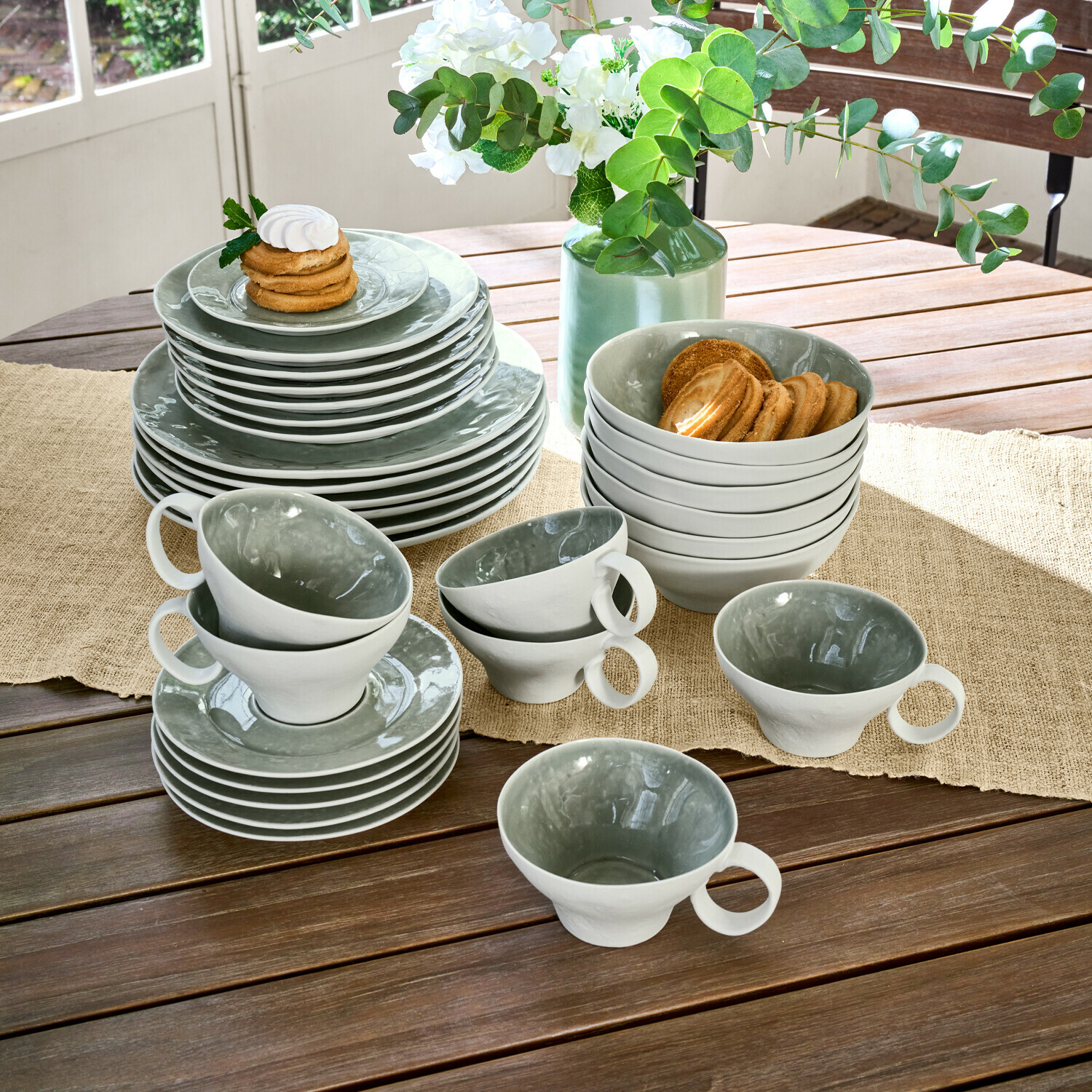 Set di 30 stoviglie Braganza Set di stoviglie in ceramica grigia e bianca su tavolo in legno con biscotti e fiori decorativi