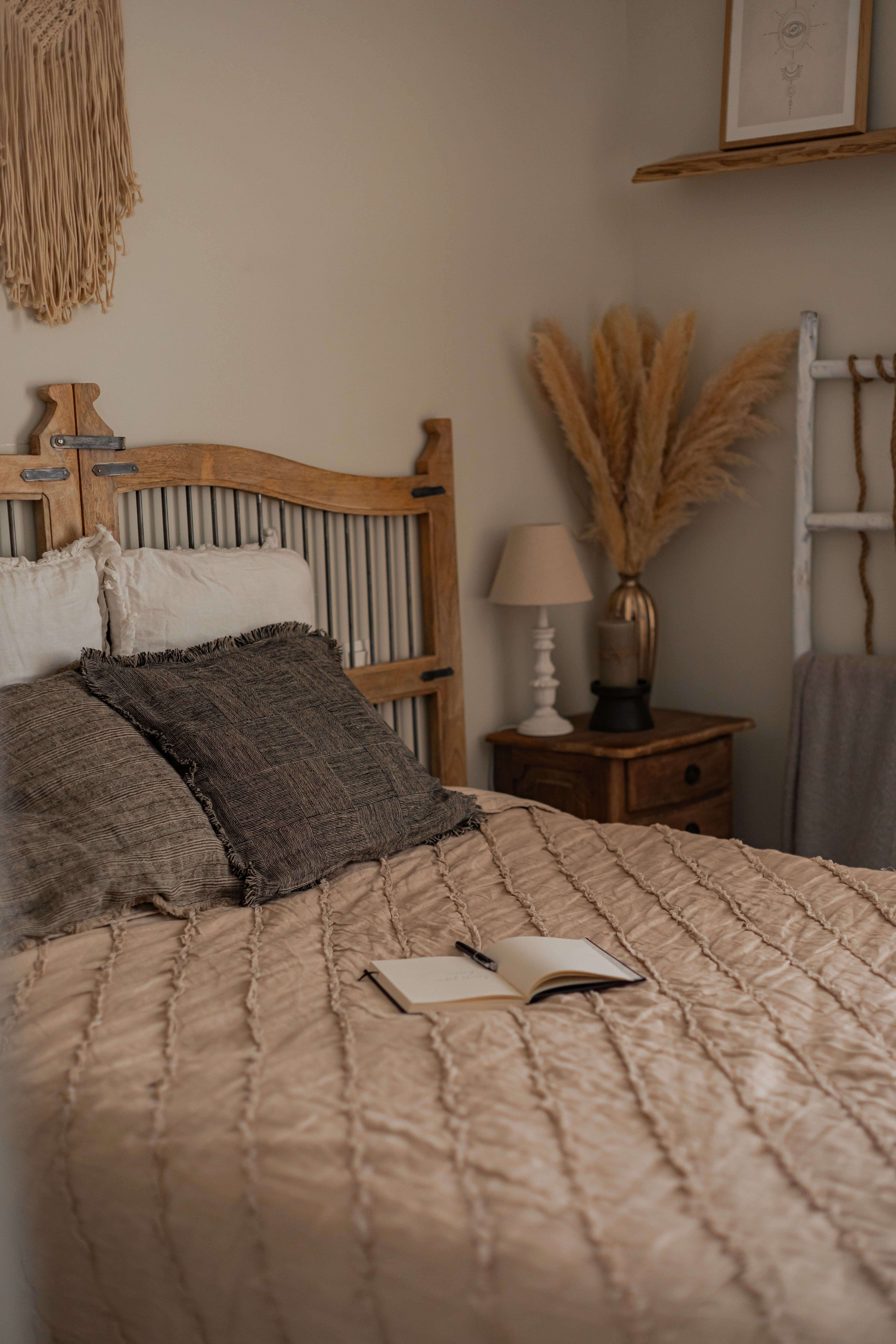 Camera da letto accogliente con letto in legno, coperta beige e decorazioni di erba della pampa