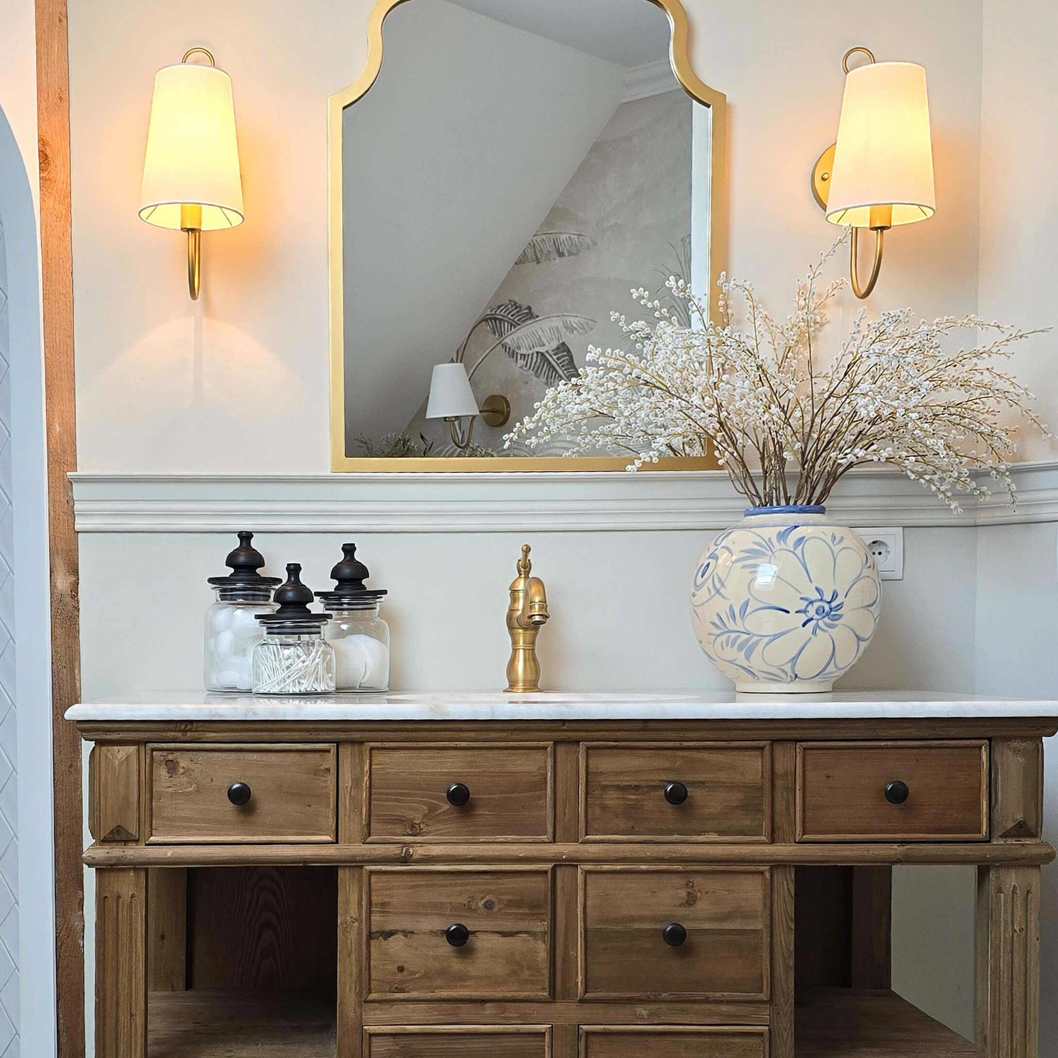 Comò in legno con piano in marmo, rubinetto dorato e vaso in ceramica blu e bianco con fiori