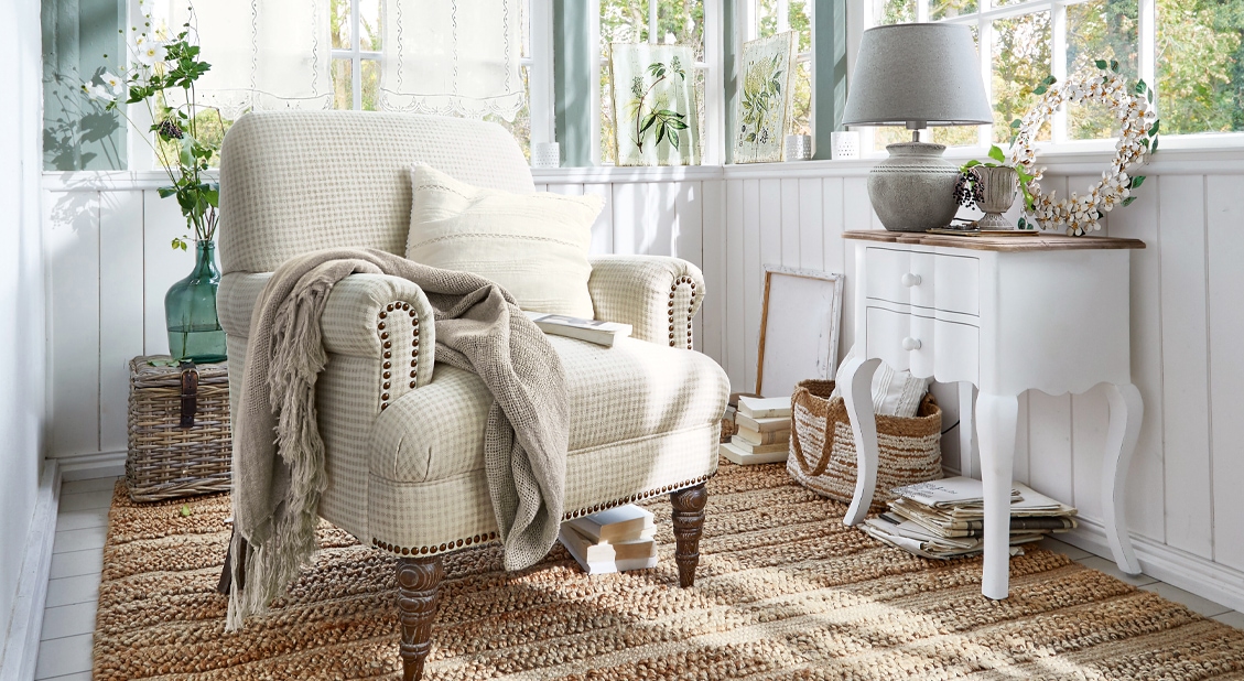 Poltrona a quadri beige con coperta e cuscino bianco in stanza luminosa con tappeto naturale