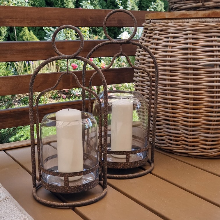 Due lanterne decorative in metallo con candele bianche su un tavolo di legno in giardino