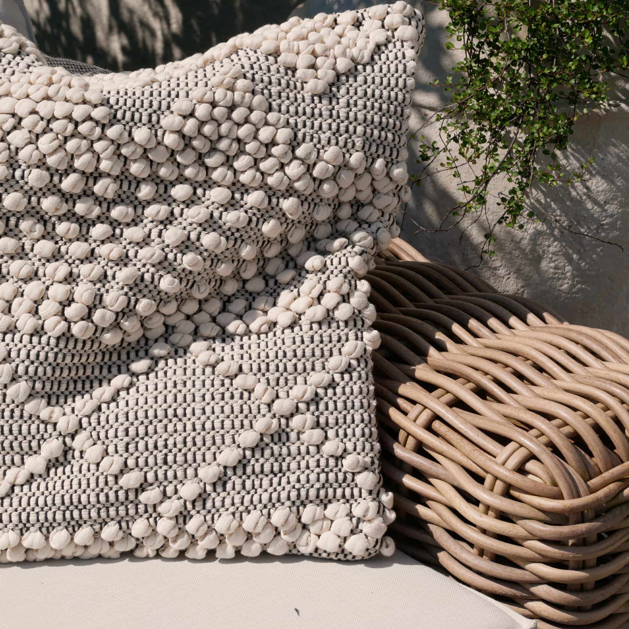 Cuscino decorativo in cotone beige e grigio su poltrona in vimini, stile boho