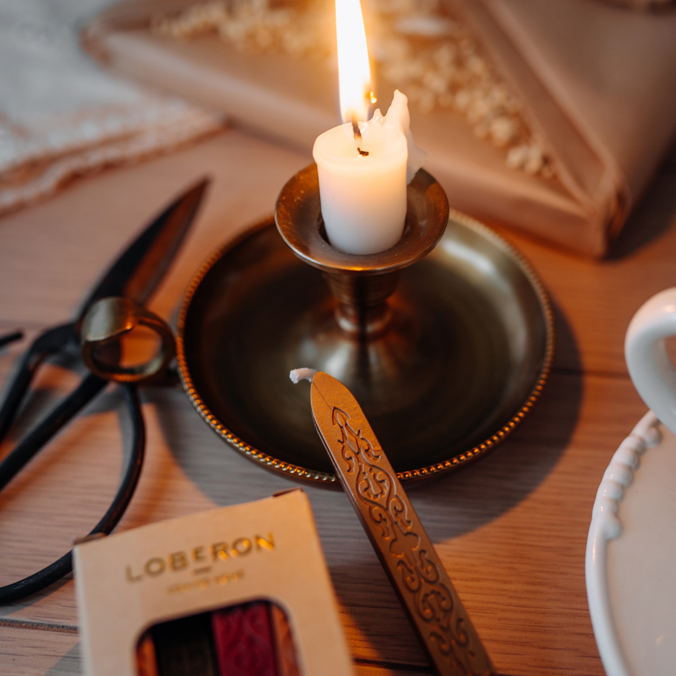 Candela bianca in portacandela di ottone con sigillo decorativo per confezionare regali e forbici