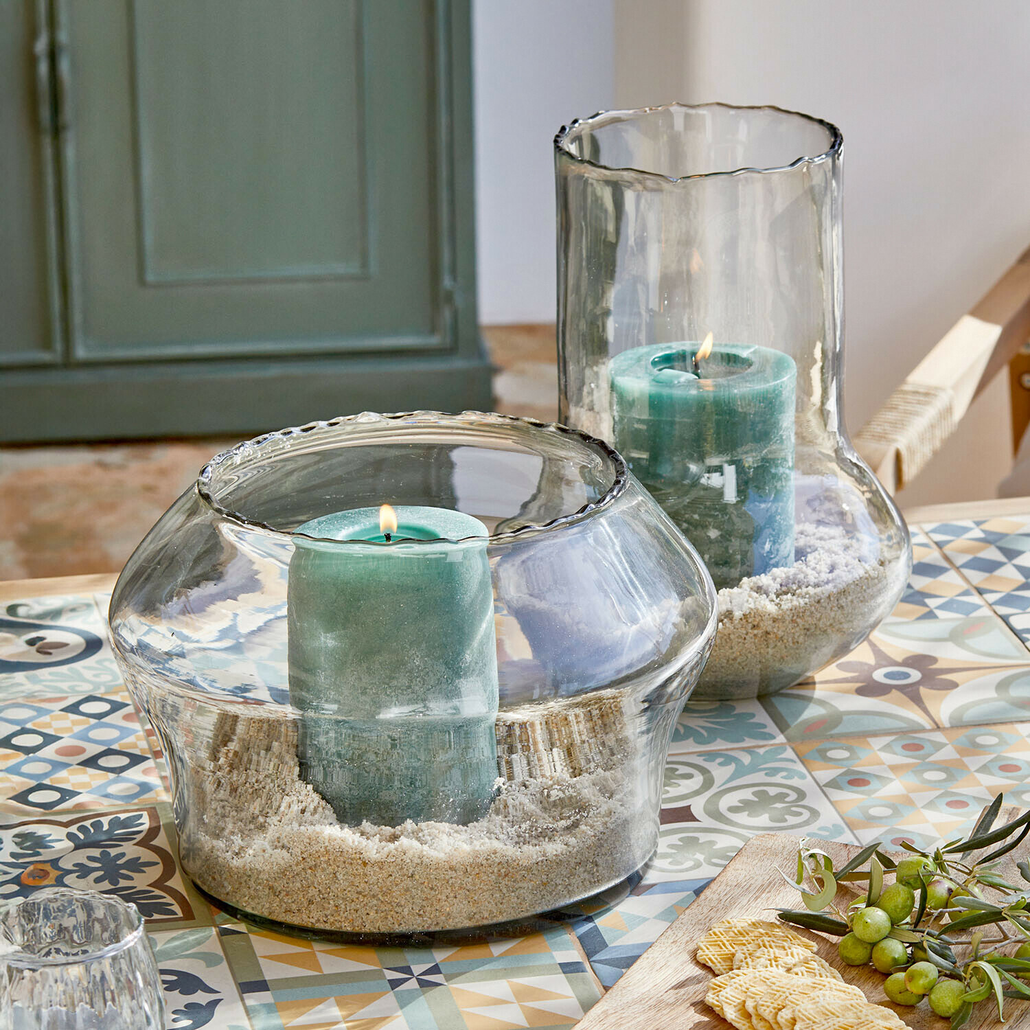 Coppia di portalumini Lumiras Portacandele in vetro con candele verdi e sabbia su tavolo colorato con motivi decorativi