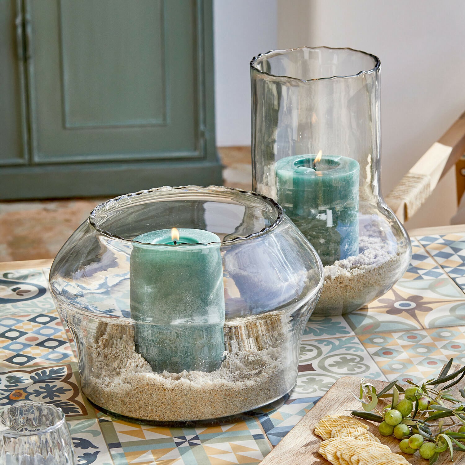 Coppia di portalumini Lumiras Portacandele in vetro con candele verdi e sabbia su tavolo colorato con motivi decorativi