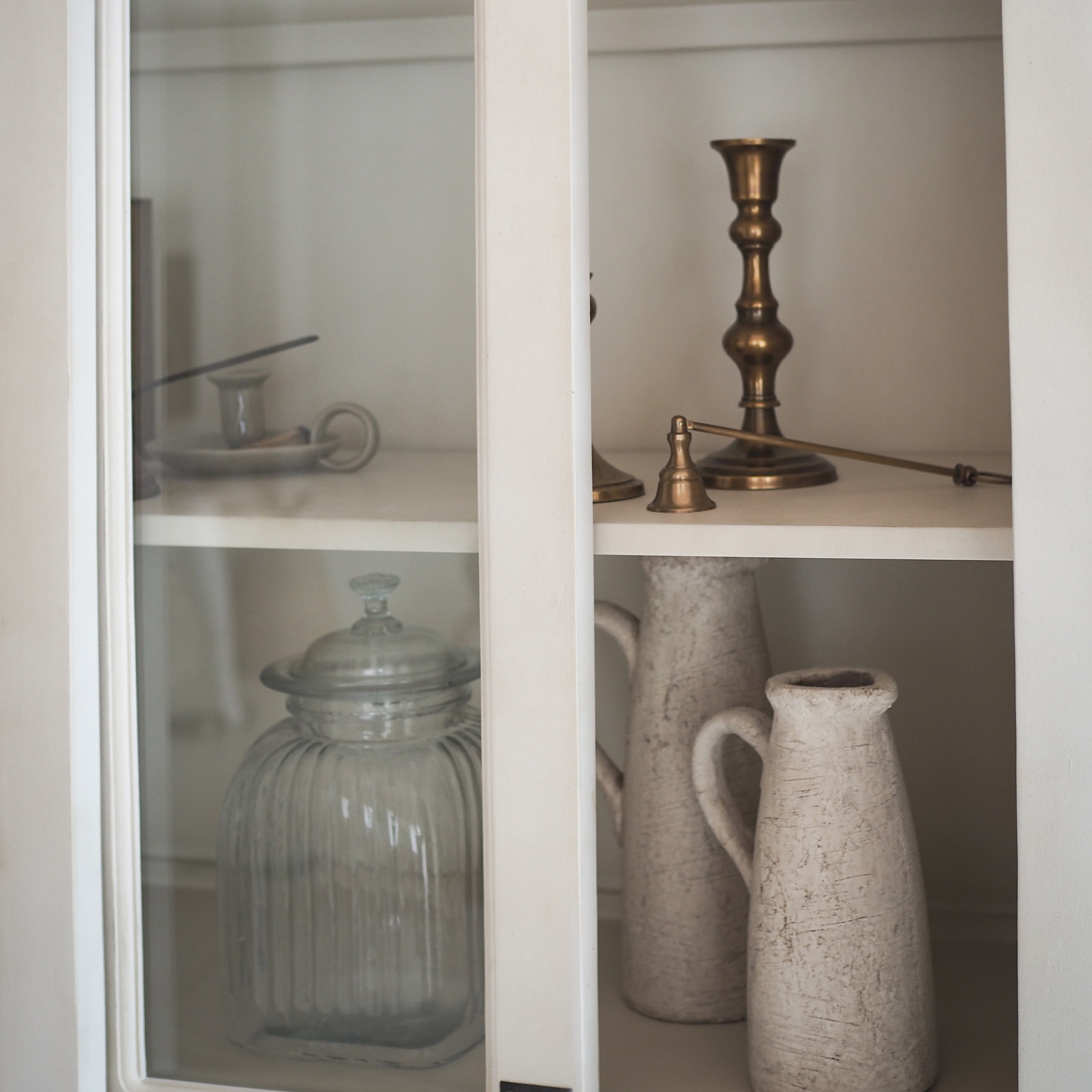 Barattolo di vetro e brocche in ceramica bianca in armadio con candelabro in ottone e campanello