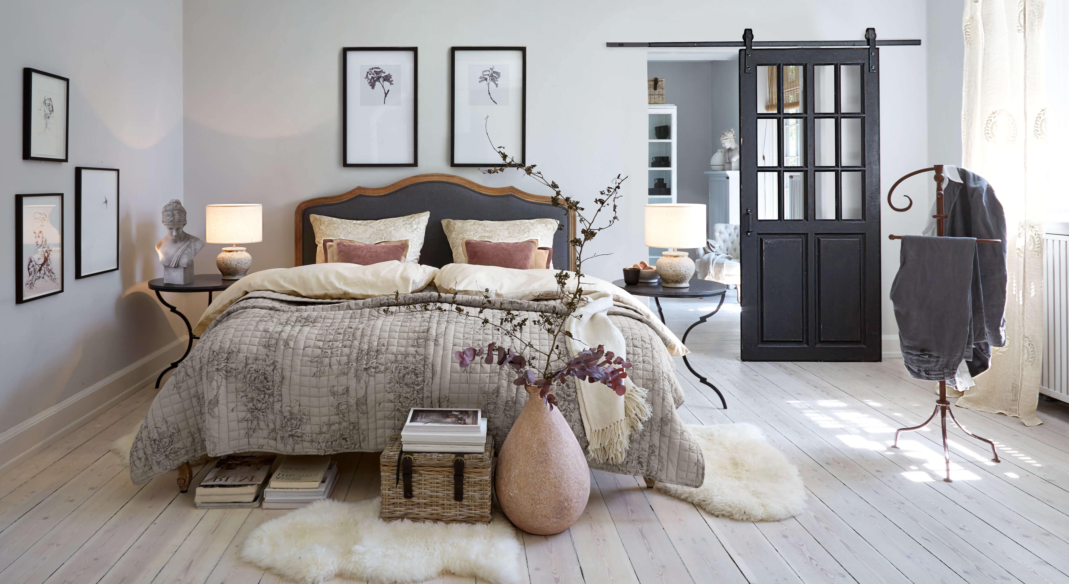 Camera accogliente con letto in biancheria grigio-beige e comodini neri con lampade