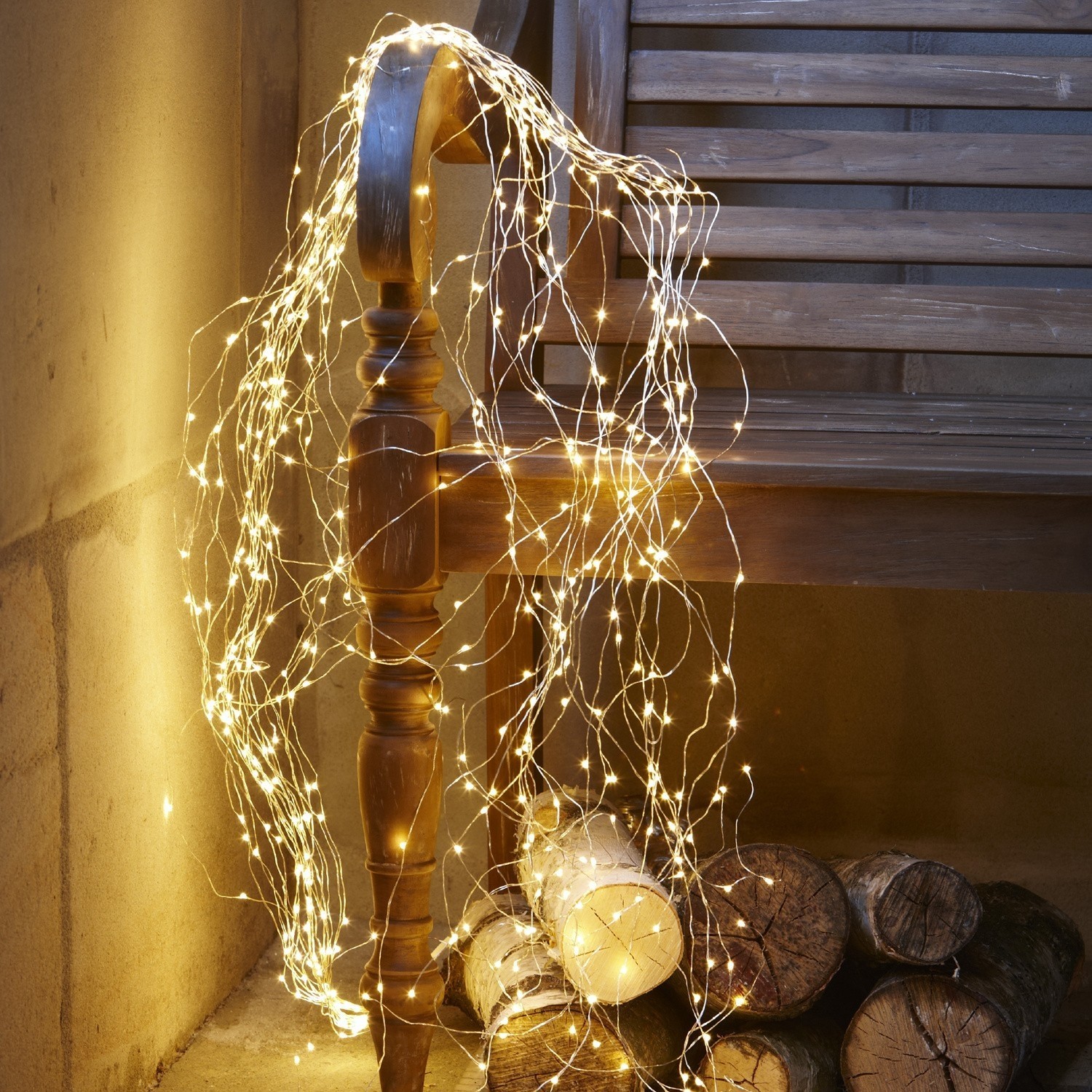 Catena luminosa Voltage Sottile catena luminosa LED a luce calda avvolta attorno a panca in legno e ceppi di legna