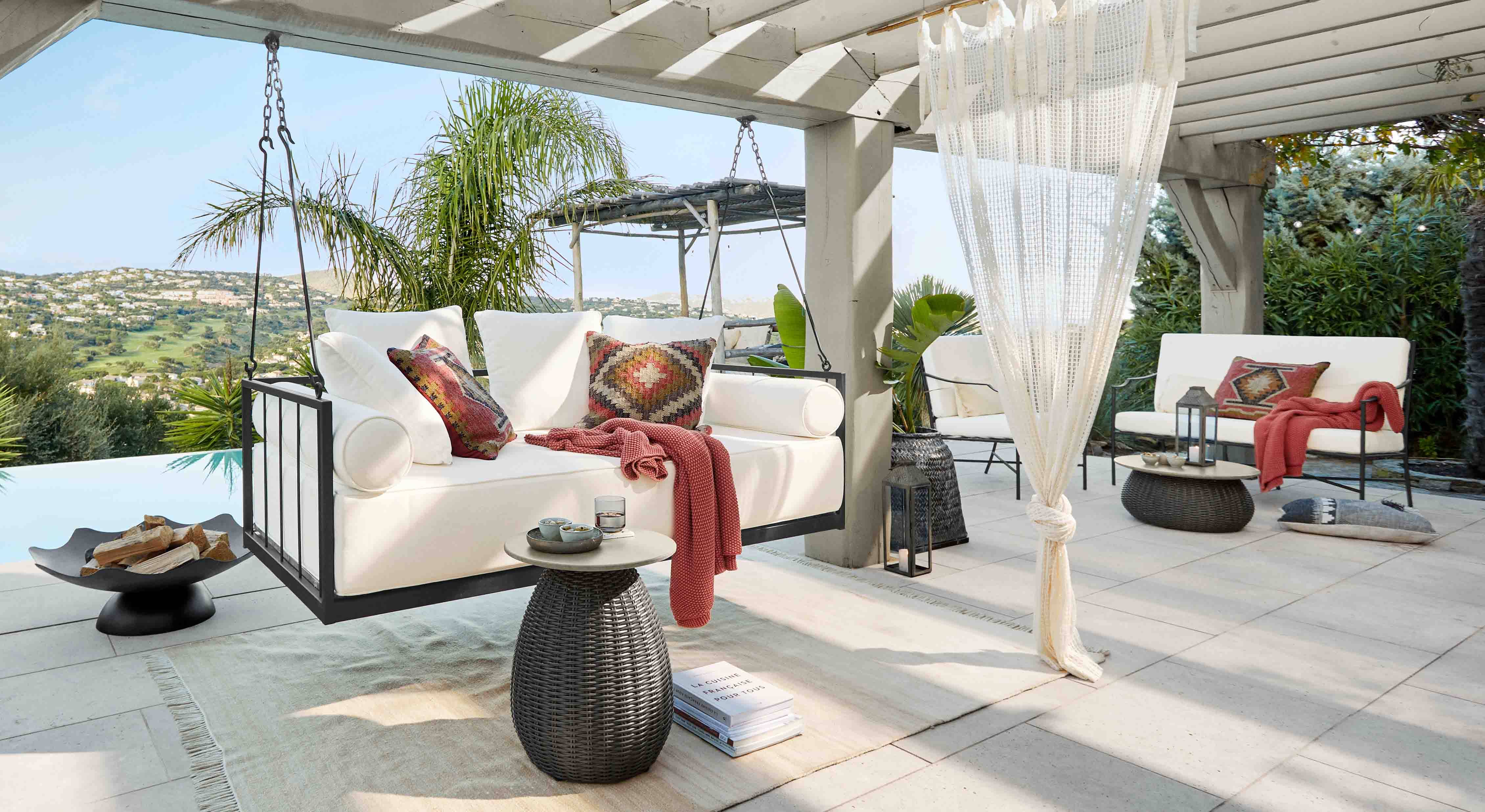 Divano sospeso bianco con struttura in metallo e cuscini colorati su terrazza con vista sulle colline