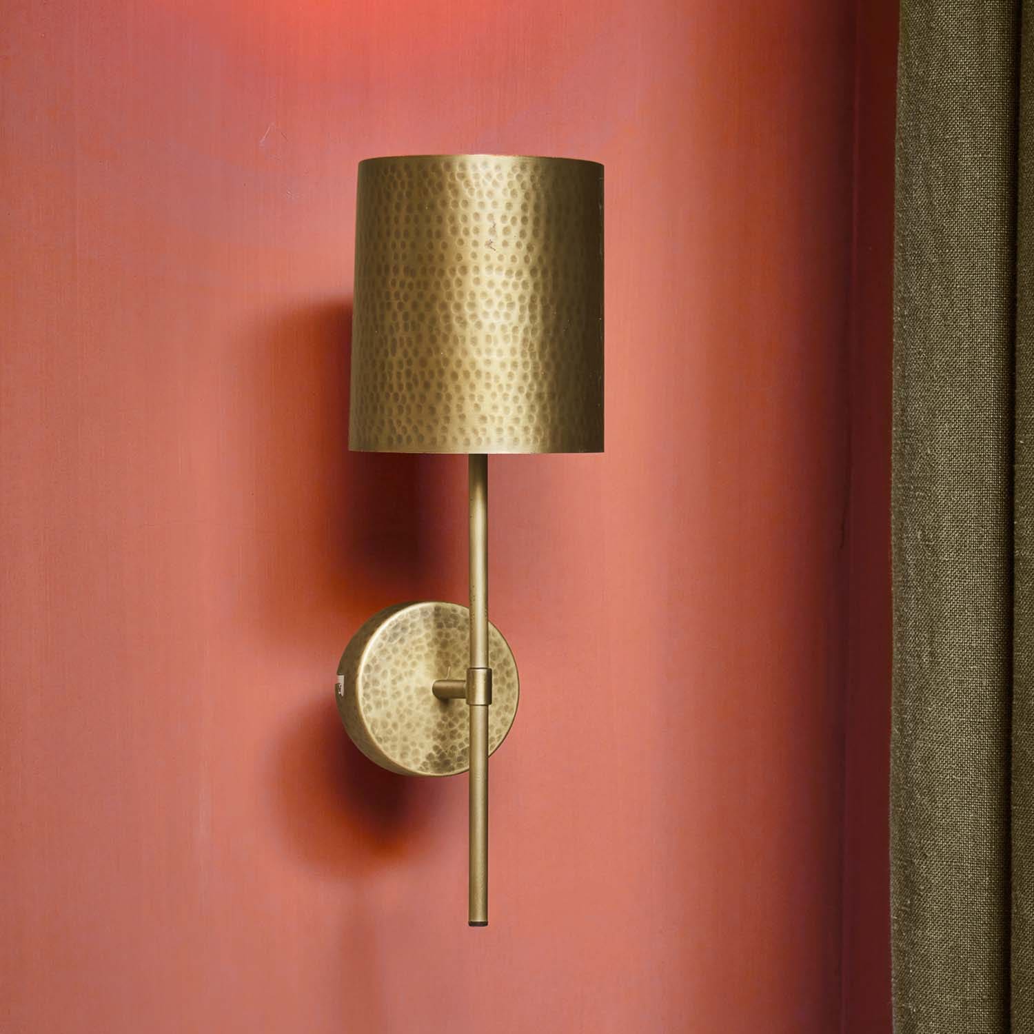 Applique in ottone martellato con paralume cilindrico su parete rossa, illuminazione decorativa