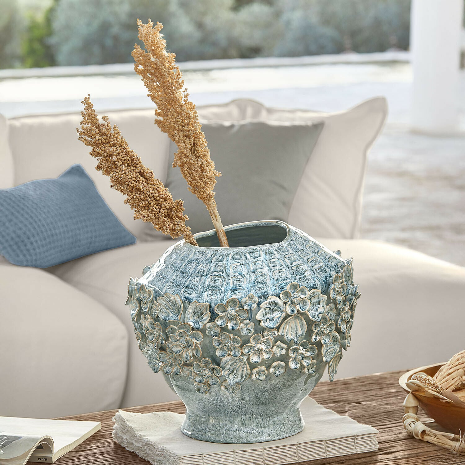 Vaso decorativo in ceramica blu con rilievo floreale su tavolo in legno in soggiorno luminoso